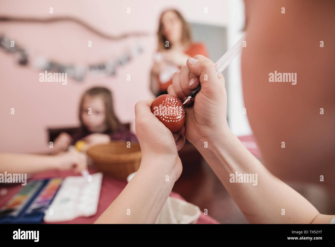 Mädchen Malerei Ostereier zu Hause mit der Familie im Hintergrund Stockfoto