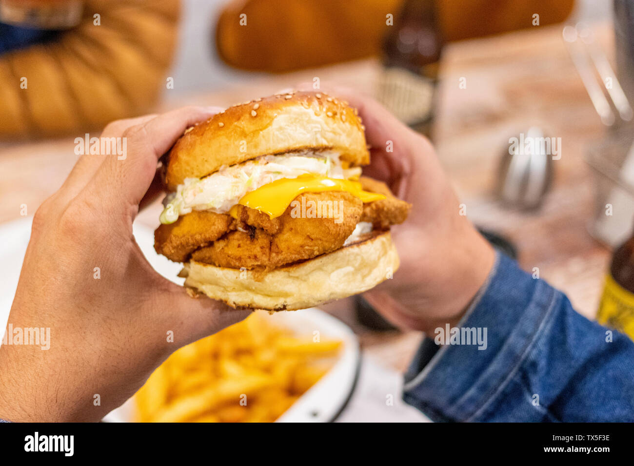 Junger Mann das Essen einer Chicken Burger mit Cheddar Käse Stockfoto