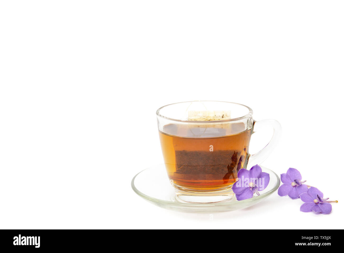 Tee Beutel in einem Glas Schale mit lila Blumen auf weißem Hintergrund. Stockfoto