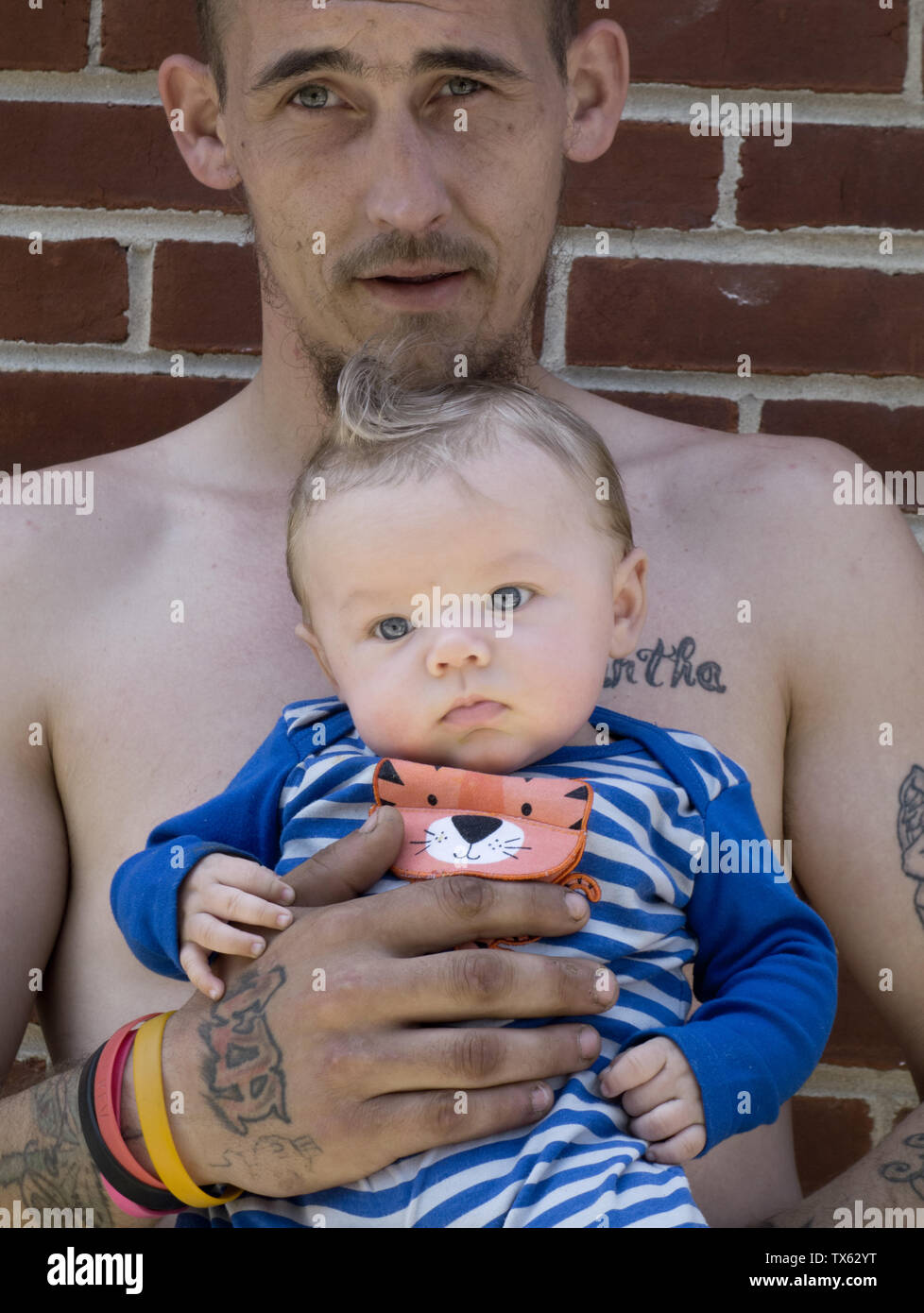 Ein Vater mit Tätowierungen hält seinen Sohn in die Arme Stockfoto