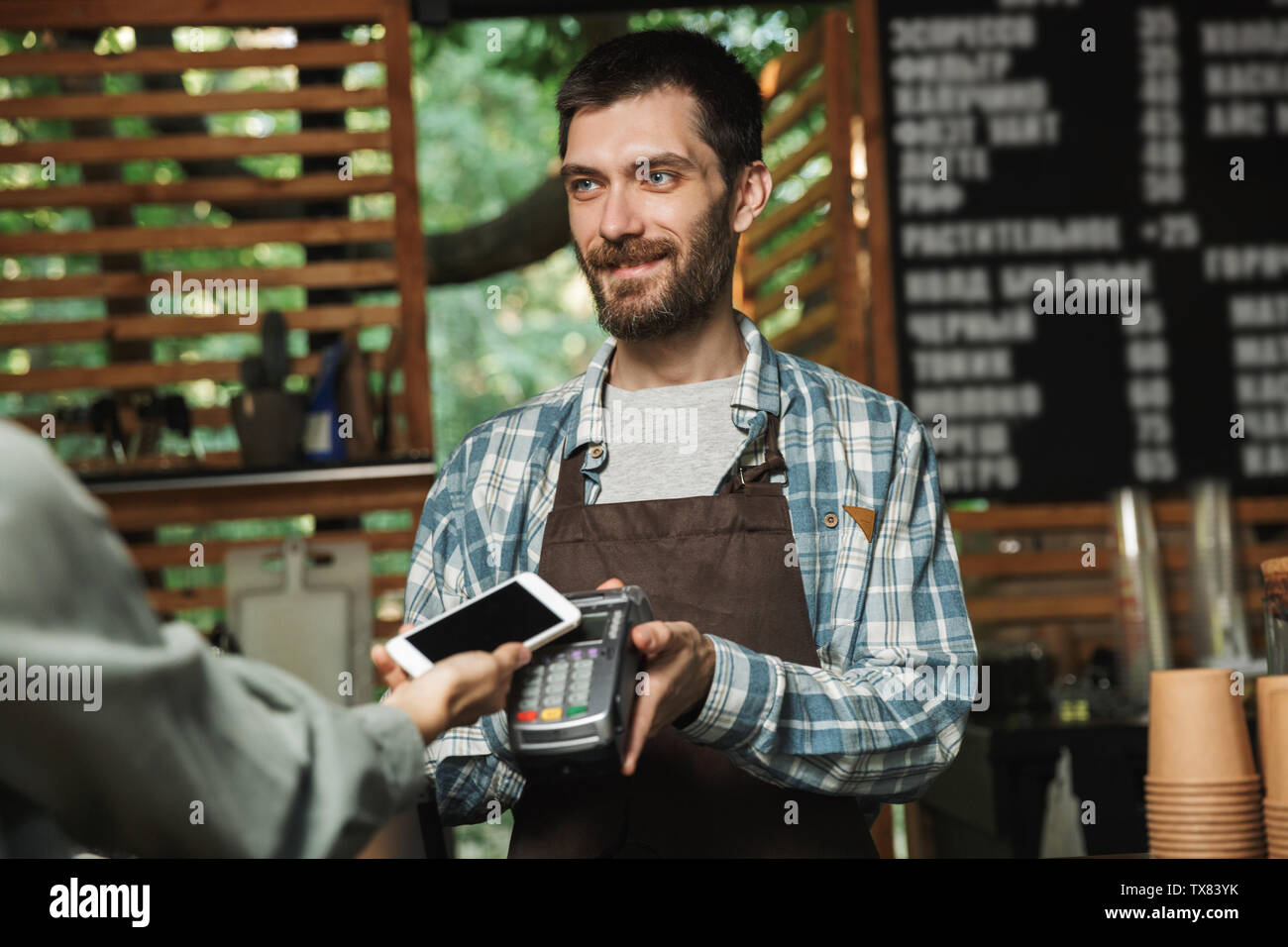 Portrait von freundlich barista Schürze mann Holding consumer Terminal für Paypass Zahlung während in Street Cafe oder Kaffeehaus Arbeiten im Freien Stockfoto
