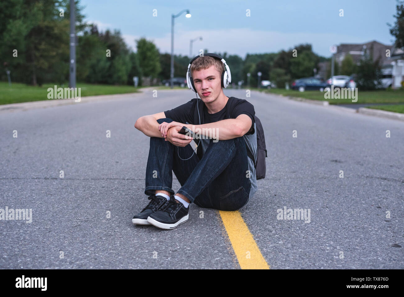 Teenager in der Mitte der Straße sitzen, während Sie Musik hören mit seinen Kopfhörern umgekippt. Stockfoto