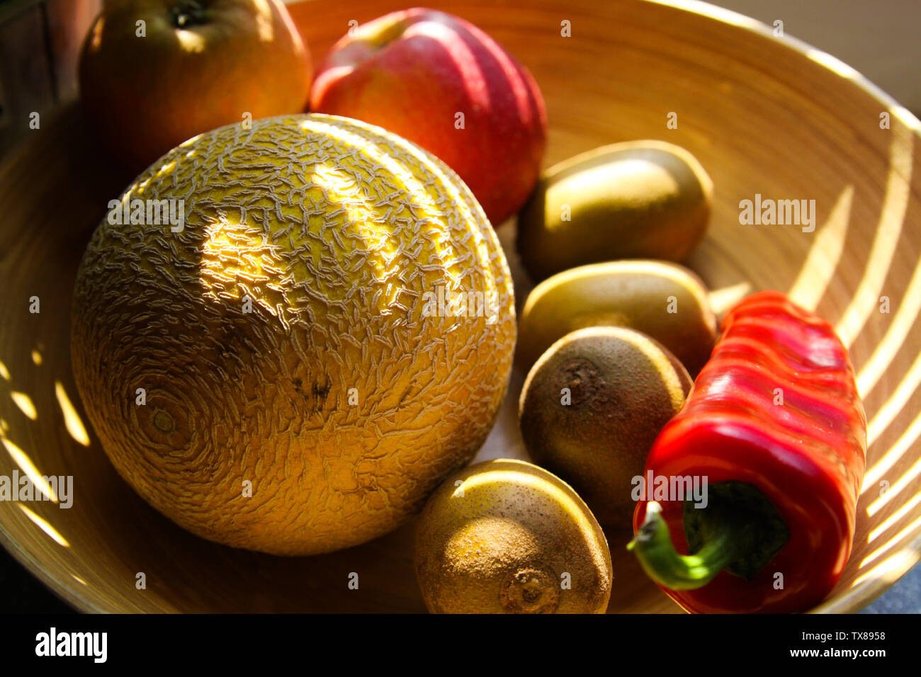 Close up Bambus Obstkorb mit Melone, Äpfel, Kiwis, Paprika von Abendsonne Balken leuchtet auf Stockfoto