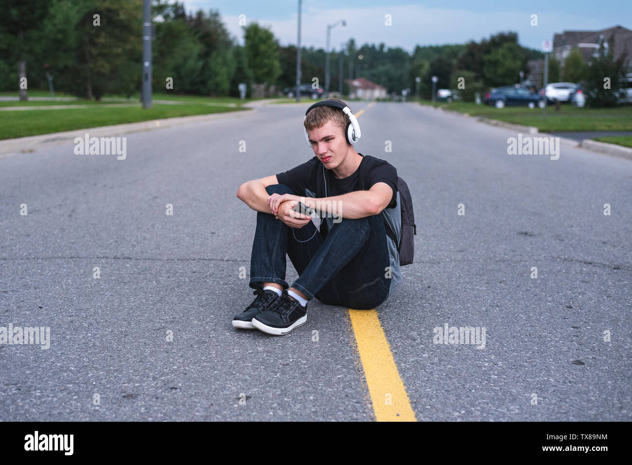 Teenager in der Mitte der Straße sitzen, während Sie Musik hören mit seinen Kopfhörern umgekippt. Stockfoto