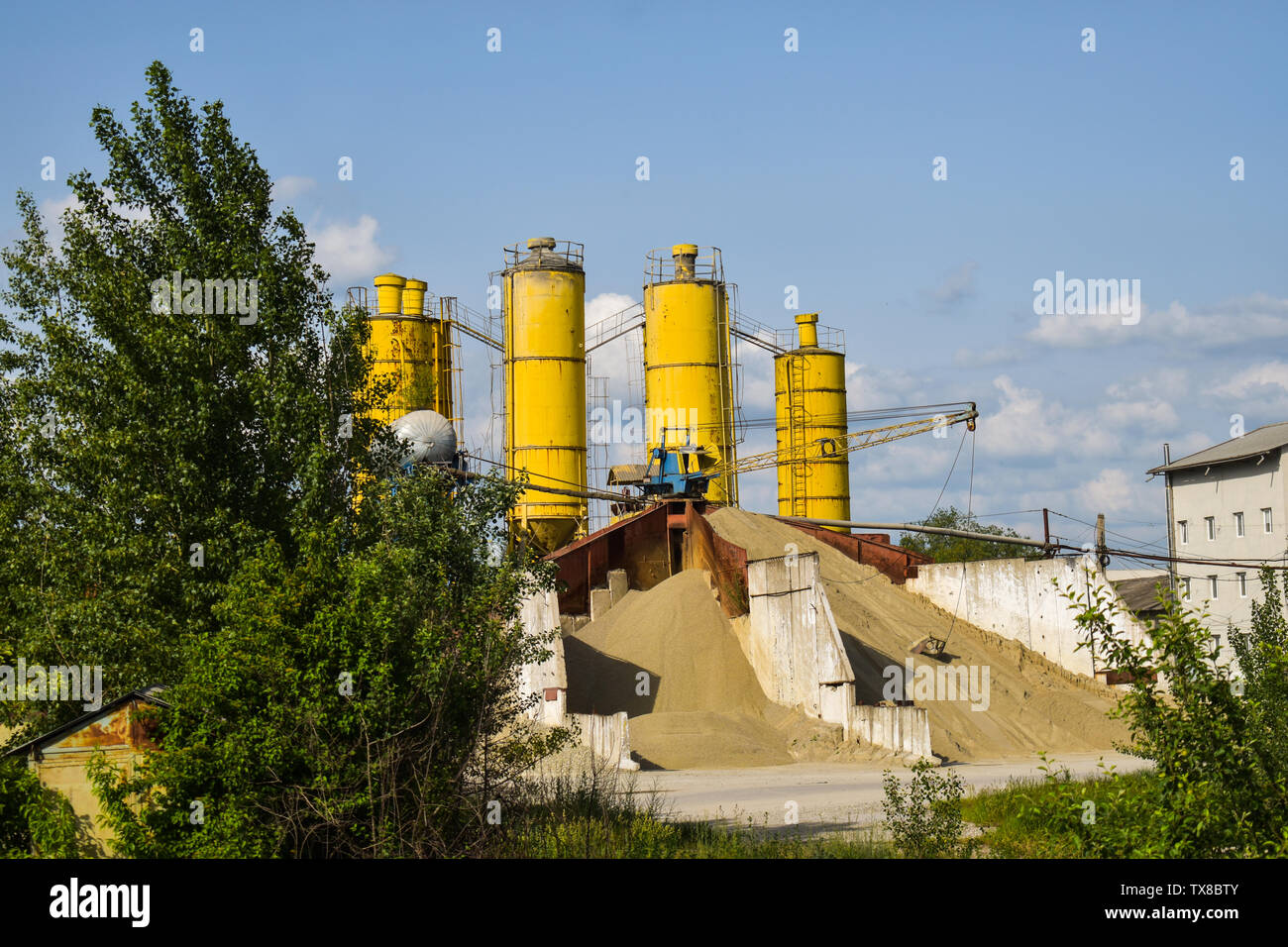 Industrielle Foto mit Haufen von Kies und Sand in der Zementfabrik mit drei grossen gelben Silo. Beton Grube für Ballast in der Zementfabrik. Stockfoto