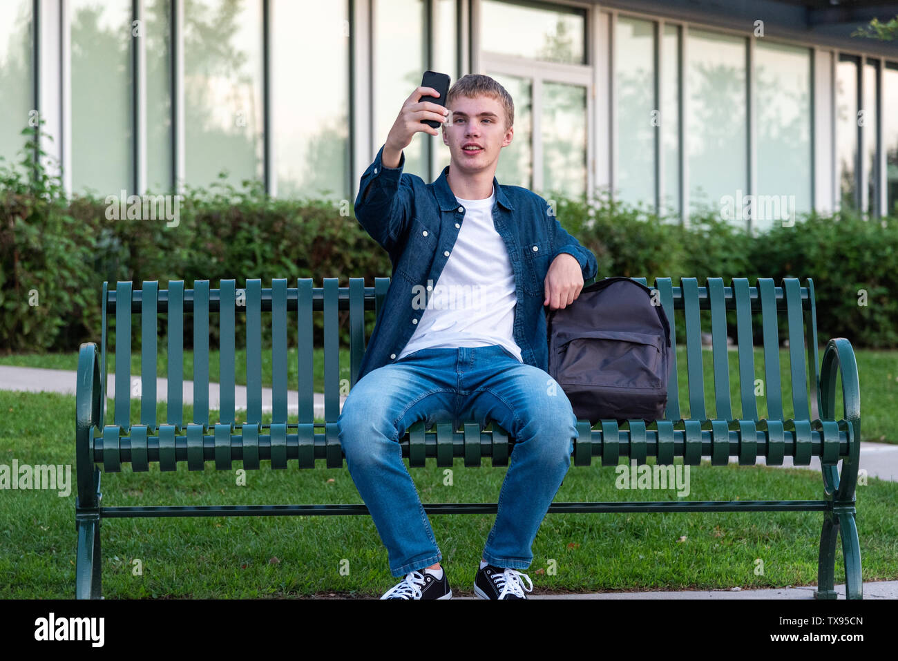 Männliche Teenager ein selfie mit seinem Telefon, während auf einer Bank sitzen. Stockfoto