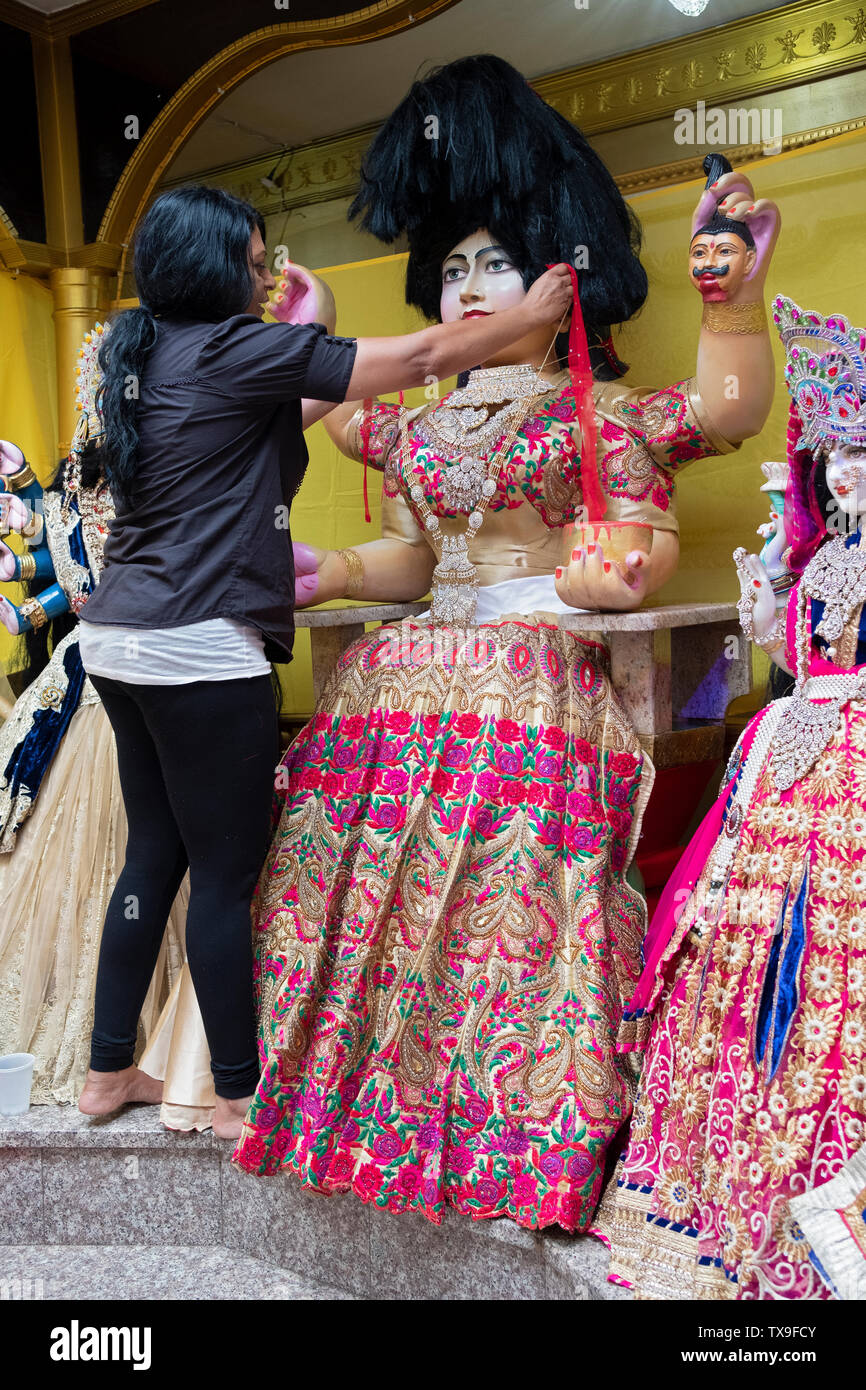 Als Teil einer Danksagung Ritual, eine fromme Frau entworfen und installiert neue Kleidung auf dem Tempel Statuen von Gottheiten. In Ozone Park, Queens, NYC Stockfoto
