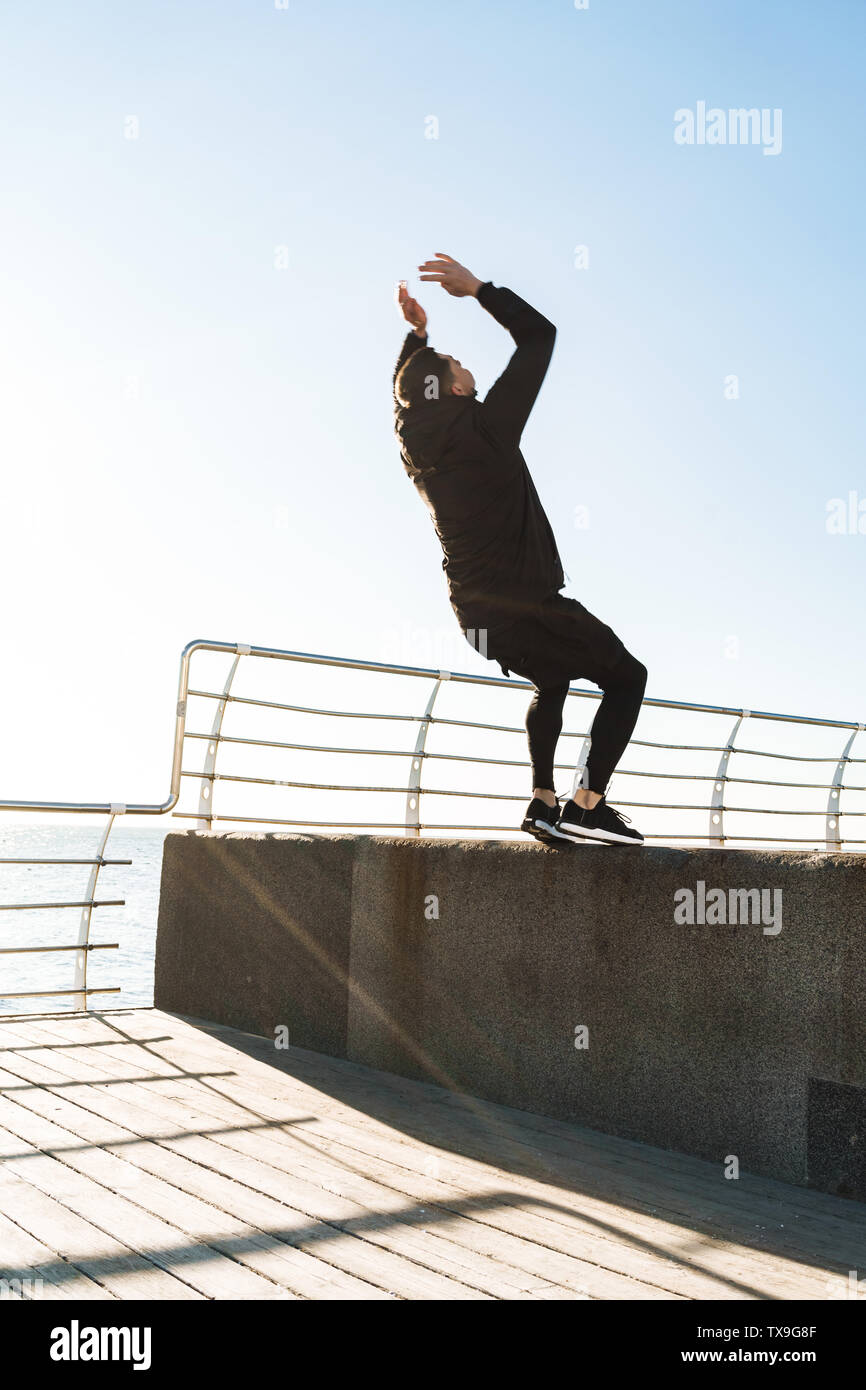 Foto von starken Kerl 20 s in schwarz Trainingsanzug, Akrobatik und springen beim morgendlichen Training von Seaside Stockfoto