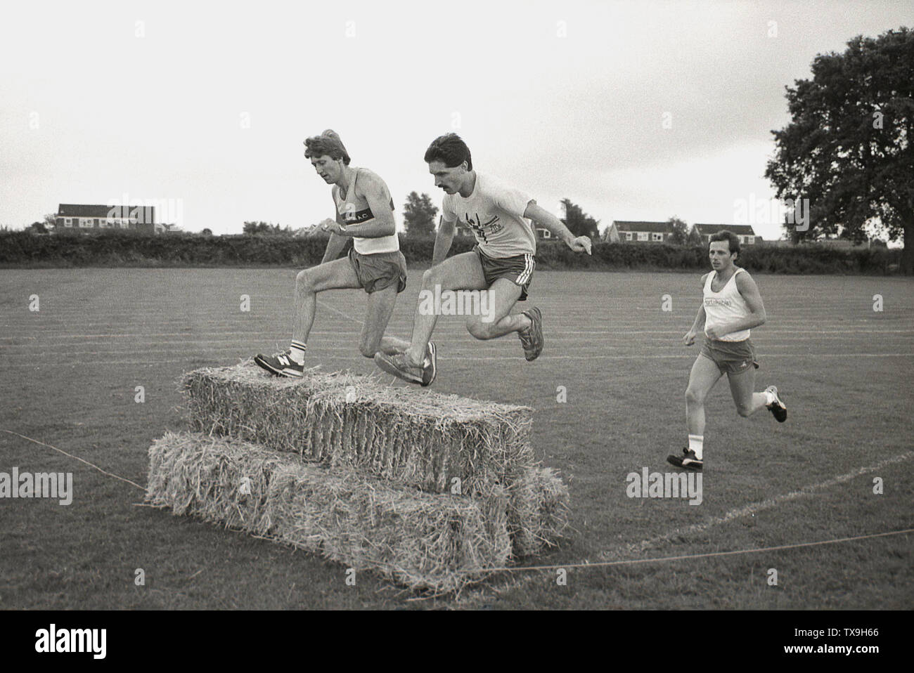 1980 s, amateur männlicher Athletik Teil in einem Hindernislauf rennen Außerhalb, in einem Feld, über Strohballen, England, UK springen. Stockfoto