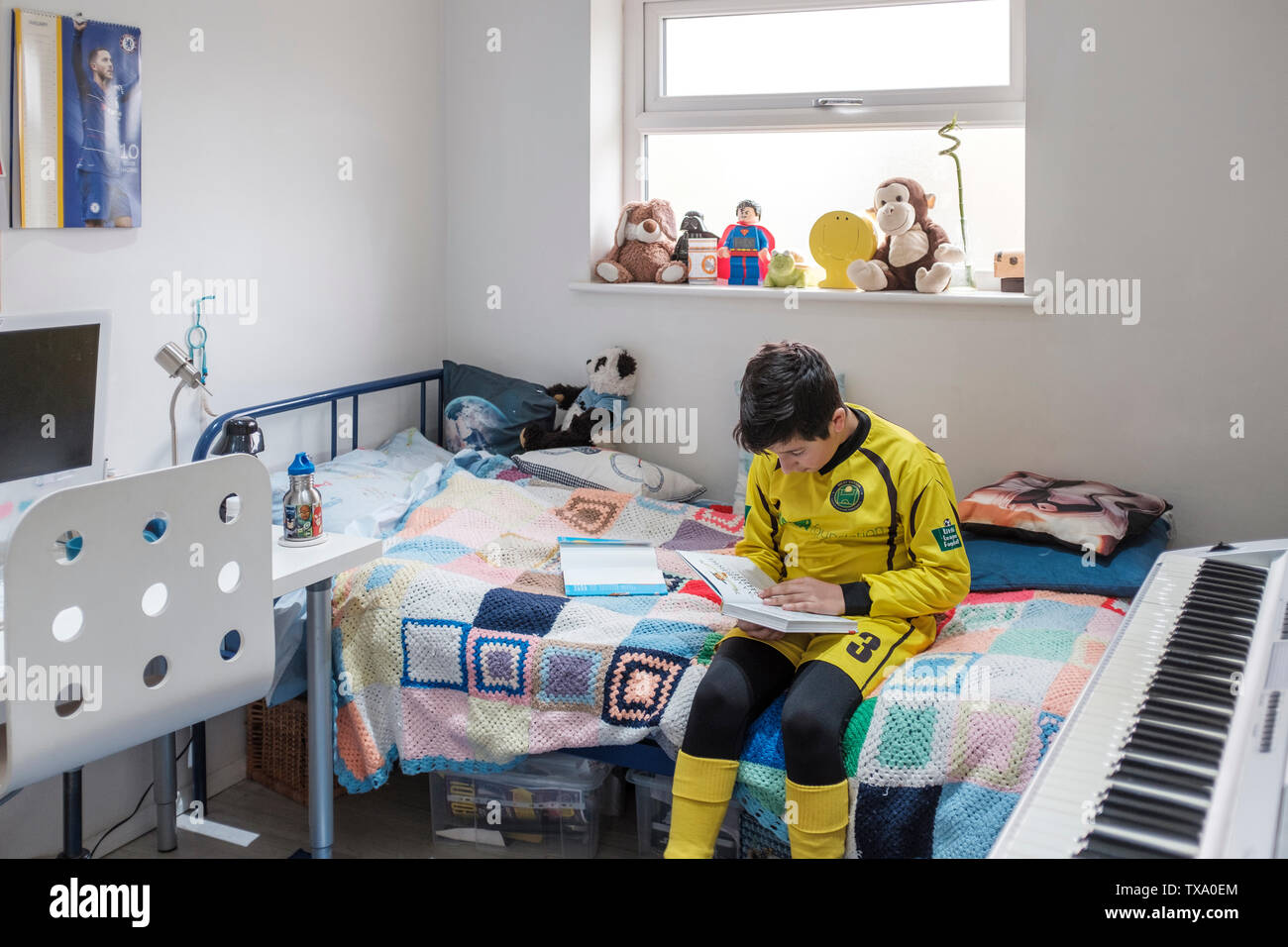 England, Uk-Young Junge, 11 Jahre in der kleinen Liga Fußball-Outfit liest ein Buch in seinem Schlafzimmer Stockfoto