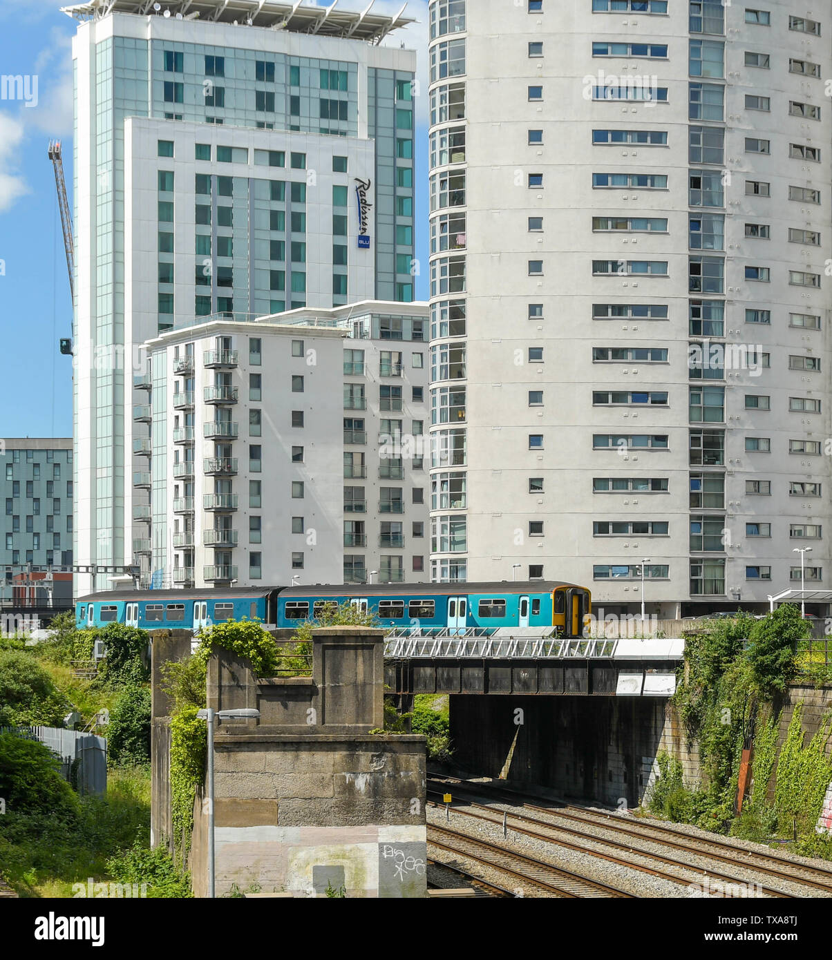 CARDIFF, WALES - JUNI 2019: Pendlerzug auf das Tal Lines Network über eine Brücke vor dem Apartment Gebäude und das Radisson Blu Hotel Stockfoto