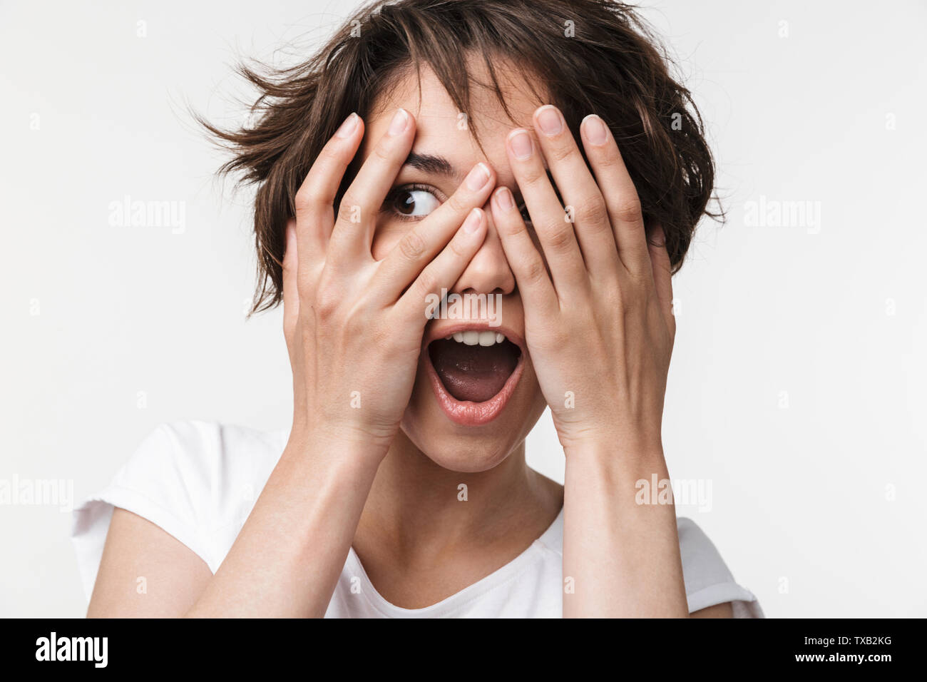 Portrait von attraktiven Frau mit kurzen braunen Haaren in Basic T-Shirt für ihre Augen mit den Händen auf weißem Hintergrund Stockfoto