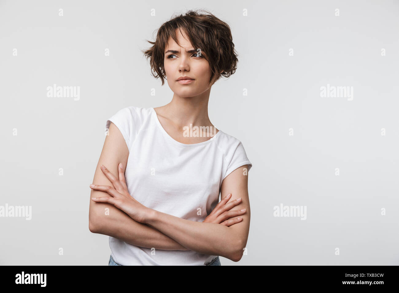 Portrait von wütende Frau mit kurzen braunen Haaren in Basic T-Shirt mit gerunzelter Stirn und Kamera auf weißem Hintergrund Stockfoto