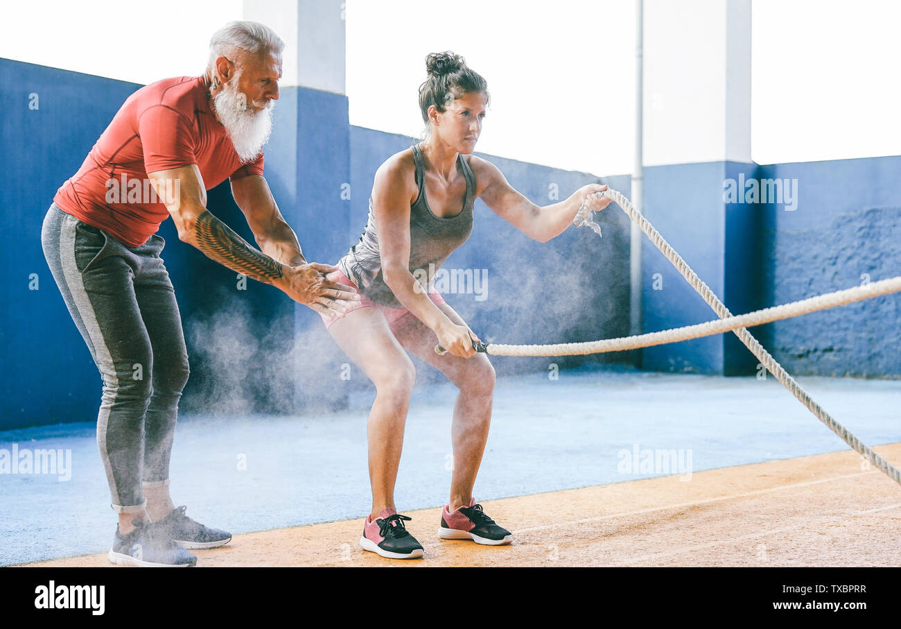 Passende Frau Training mit Schlacht Seil im Fitnessstudio - Hipster personal trainer Motivieren einer weiblichen Athleten wer tut Ausdauerübungen Stockfoto