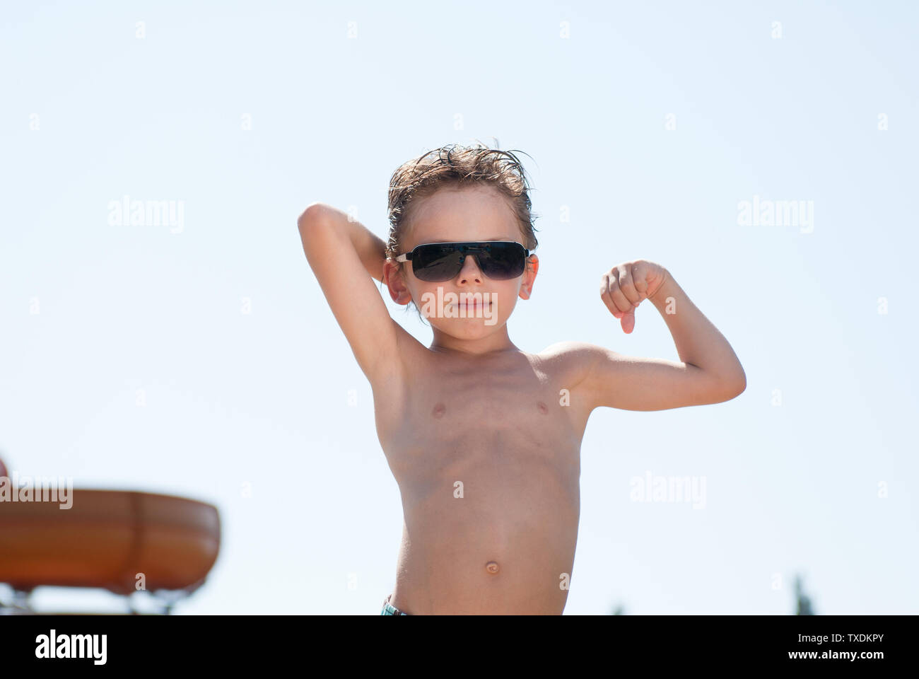 Gesunden kleinen Jungen mit brauner Haut in Sonnenbrille Sonnen in Wasser Sommer Park zeigt starke Muskel Stockfoto