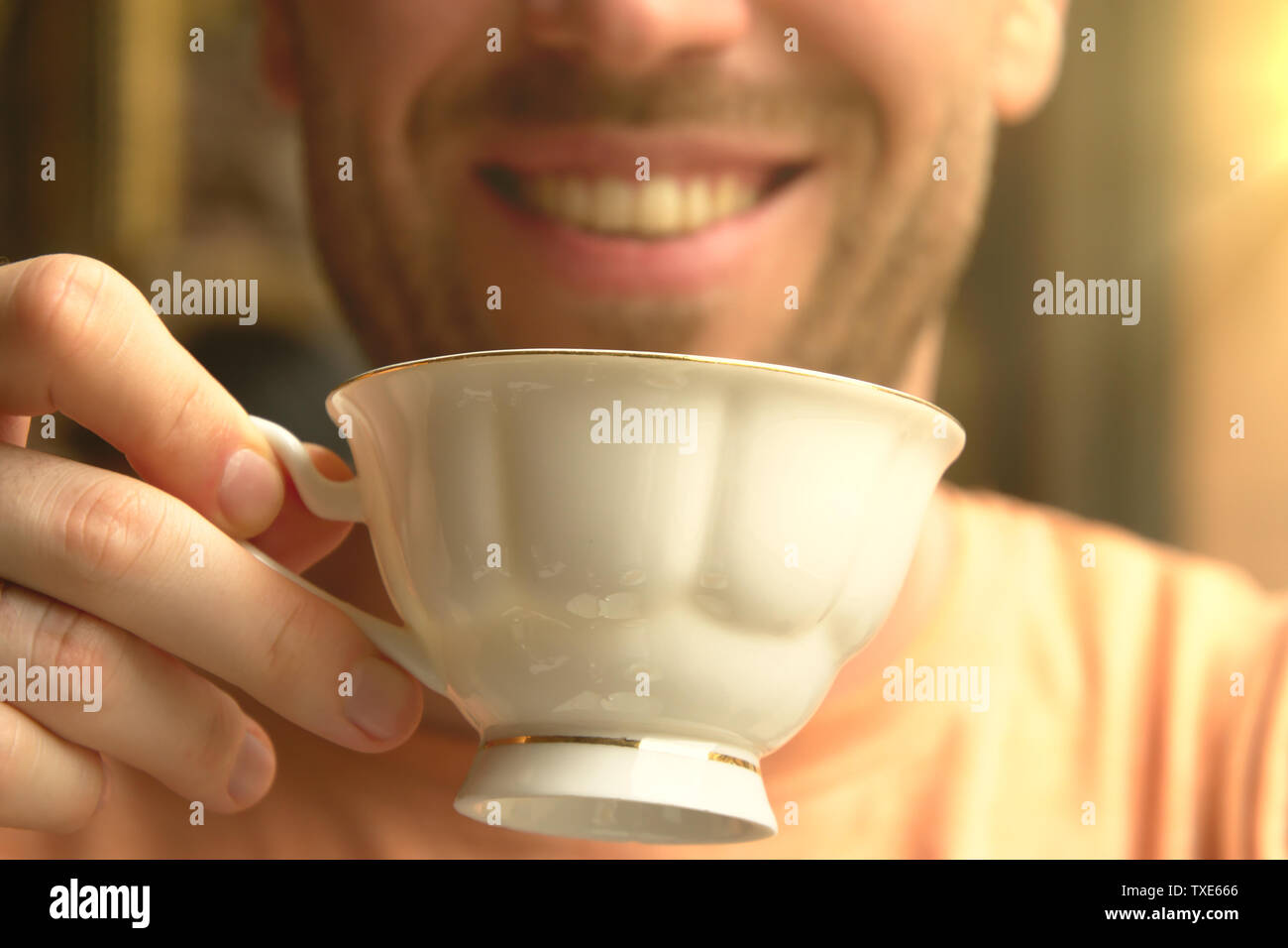 Die lächelnden Mann Getränke auf Tee- und hält die Schale in die Hände in den weichen Sonnenlicht im Cafe Stockfoto