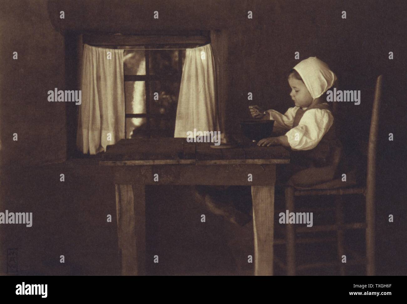 Hunger ist der Beste Koch. Foto datiert 1898 von Myra Albert Wiggins, 1869-1956; zeigt ein kleines Mädchen, trägt eine Mütze und Holzschuhe, sitzend auf einem hohen Stuhl an einem Holztisch essen aus einer Schüssel. Stockfoto
