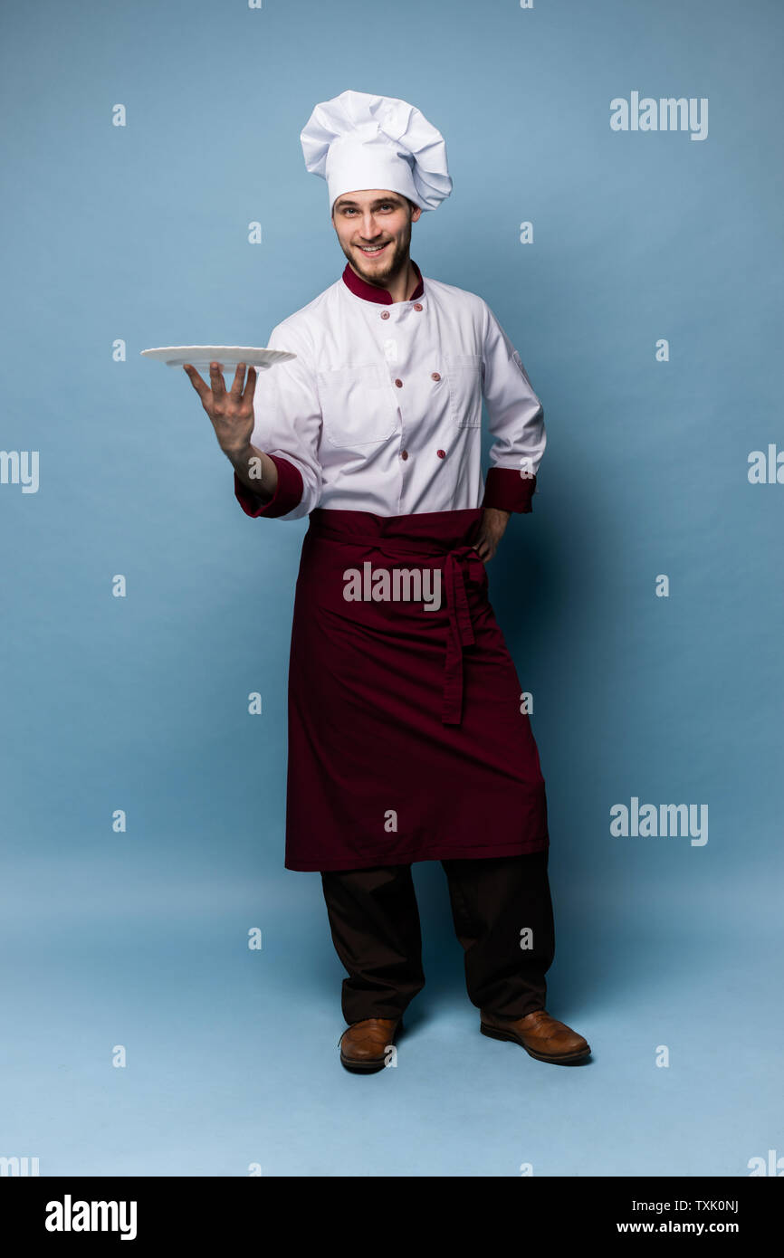 Gerne männliche Küchenchef stehend mit Platte auf hellblauem Hintergrund isoliert. Stockfoto
