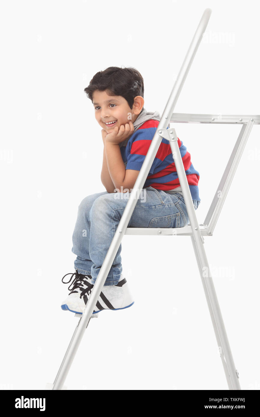 Junge sitzt auf einer Leiter und lächelnd Stockfoto