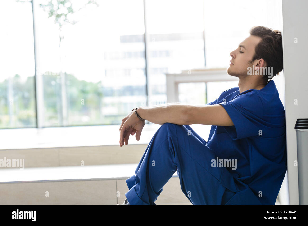Junge männliche junior Arzt sitzen auf dem Boden im Krankenhaus Flur Stockfoto