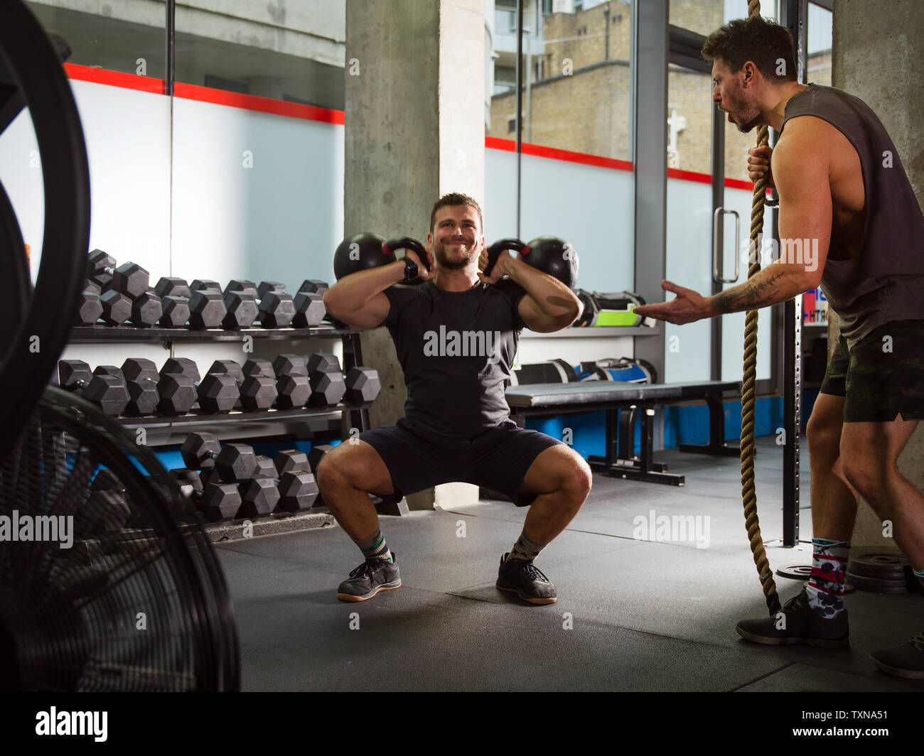 Mann motivierender Freund hockt, heben Kettlebells in der Turnhalle Stockfoto