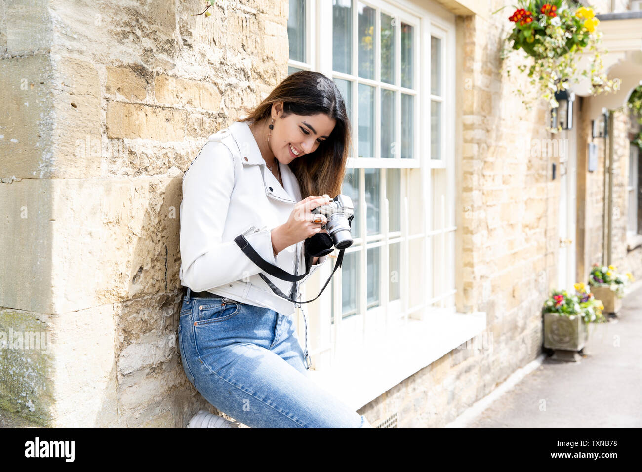 Junge Frau gegen Straße Wand lehnt Überprüfung Fotos Digitalkamera, Cotswolds, England Stockfoto