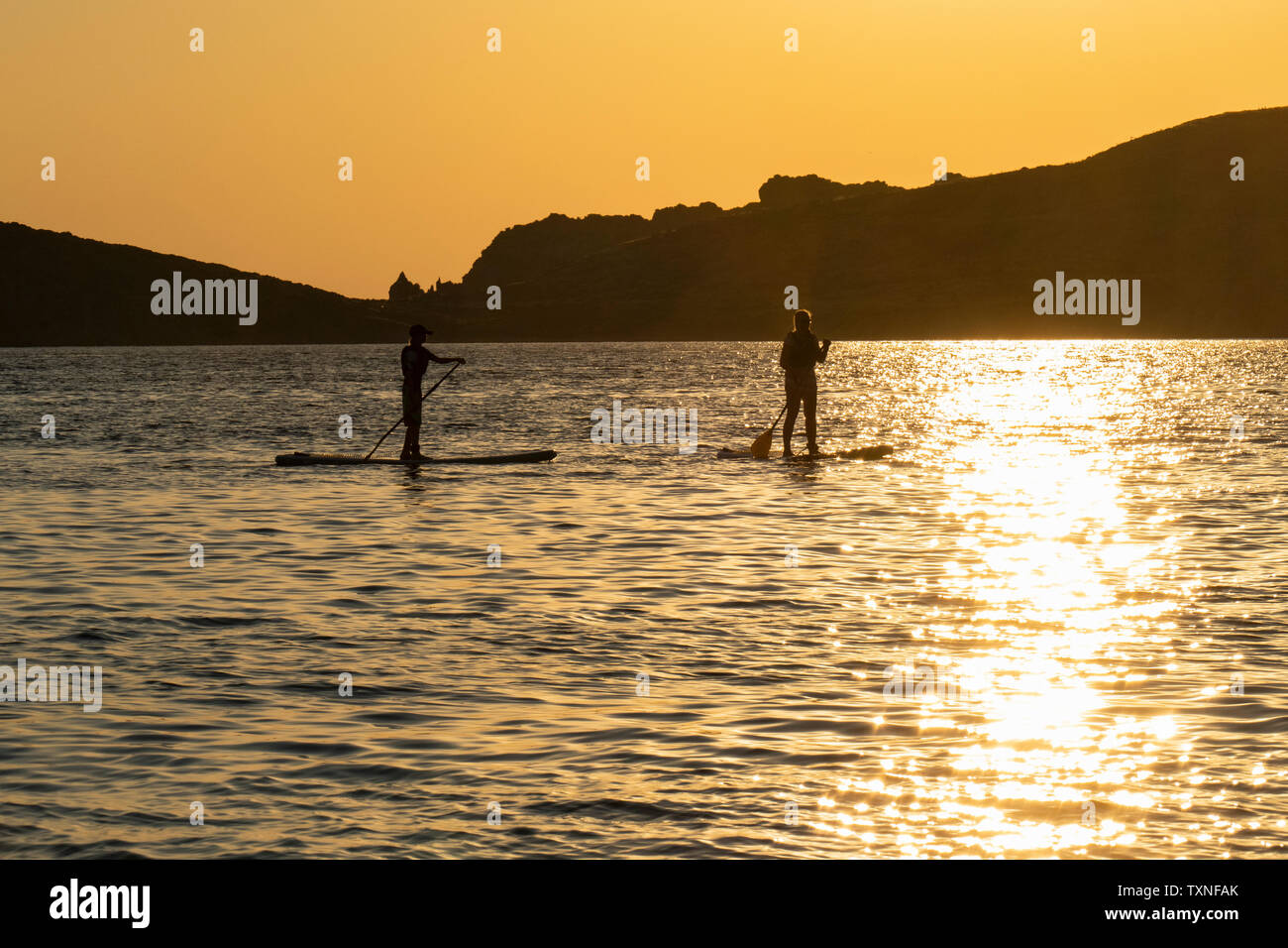 Mutter und Sohn standup paddleboarding im Meer bei Sonnenuntergang, Limnos, Chios, Griechenland Stockfoto