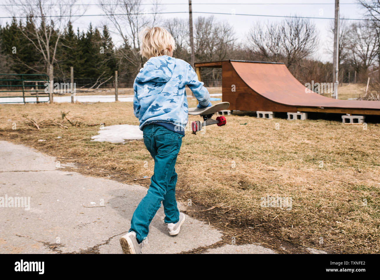 Blonde Junge mit Skateboard in Richtung ländliche Skateboard-rampe, Rückansicht Stockfoto