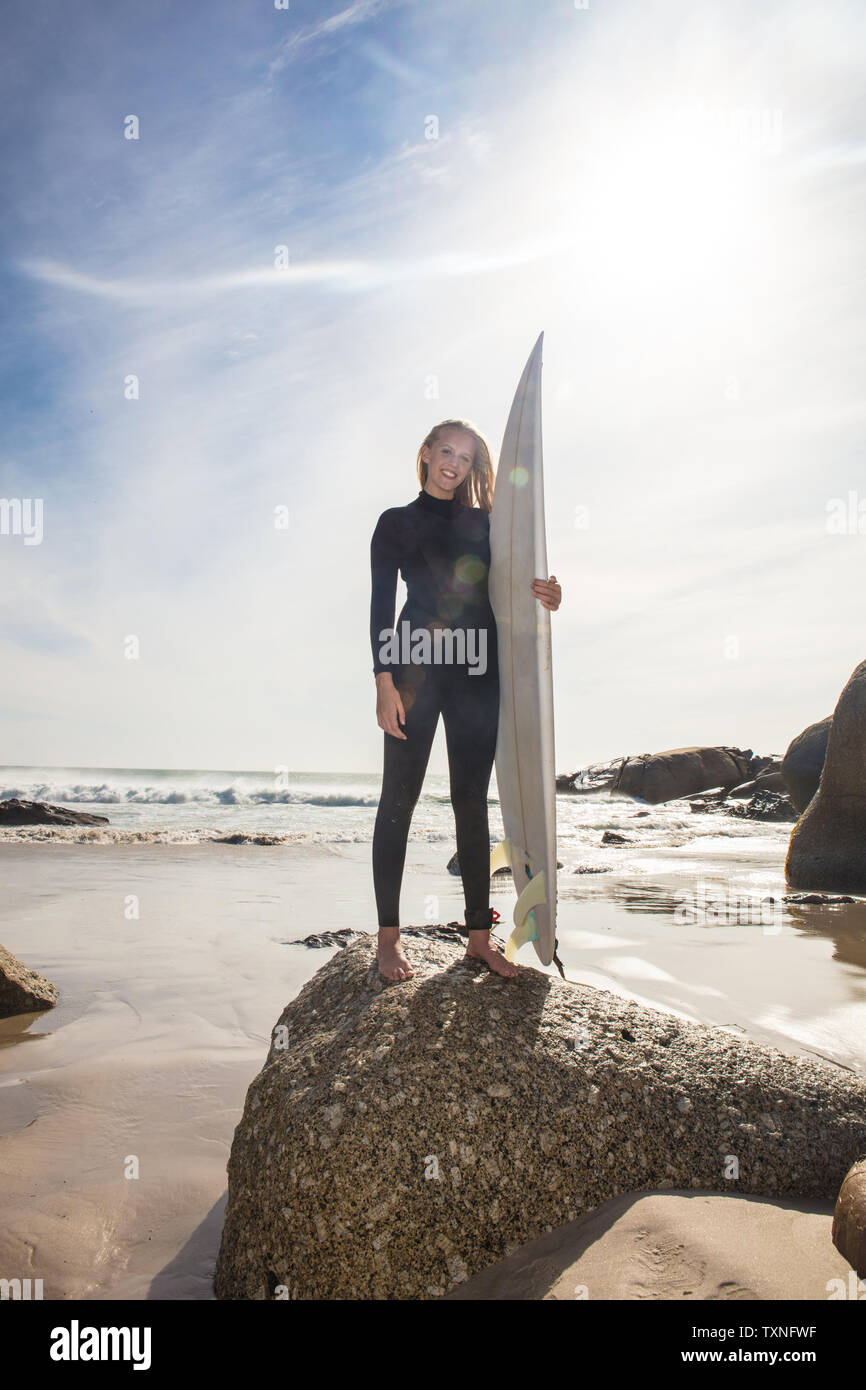 Junge weibliche Surfer, Surfbrett am Strand Felsen, in voller Länge Porträt, Cape Town, Western Cape, Südafrika Stockfoto