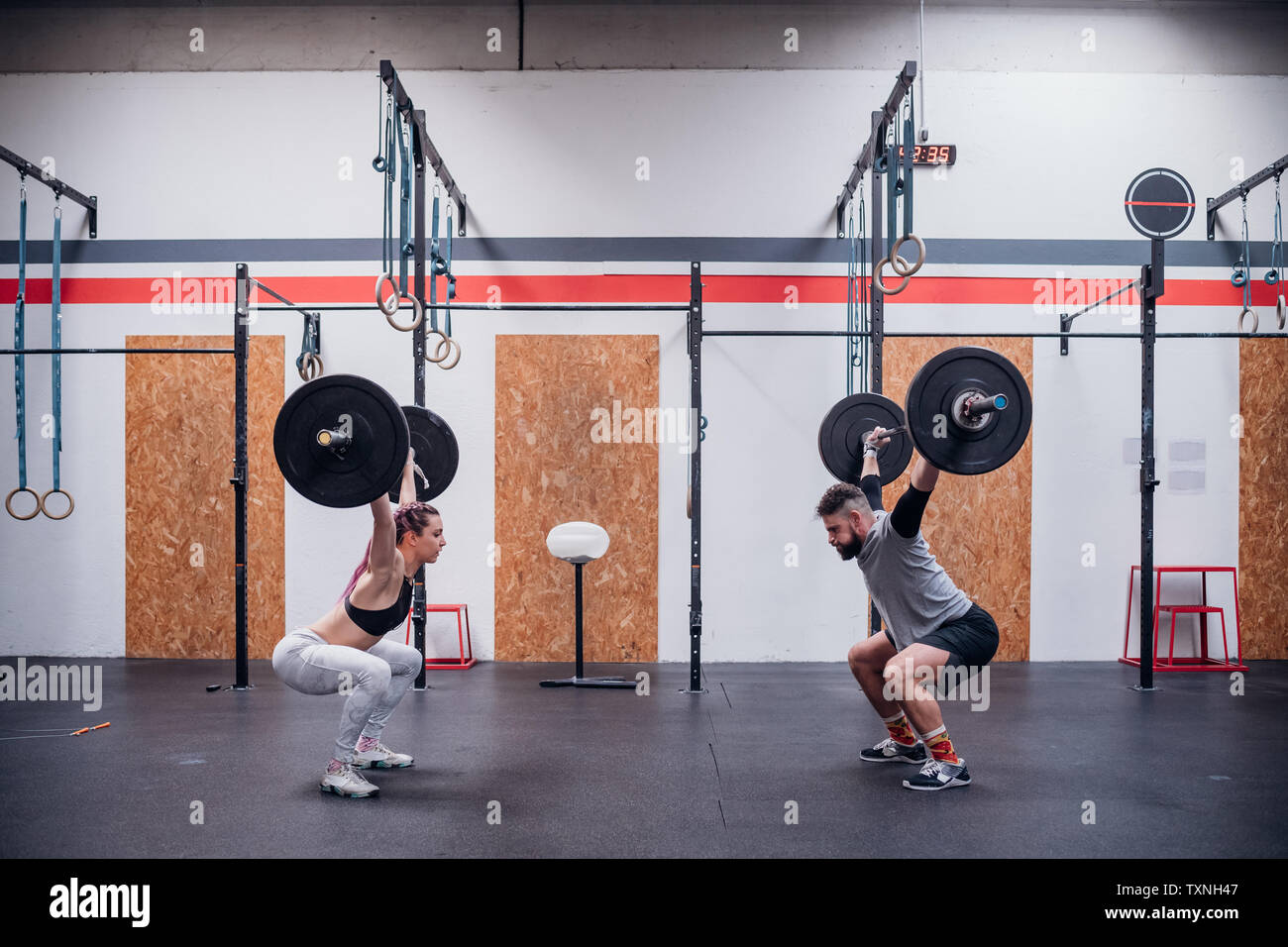 Junges Paar hocken und Anheben barbell in der Turnhalle Stockfoto