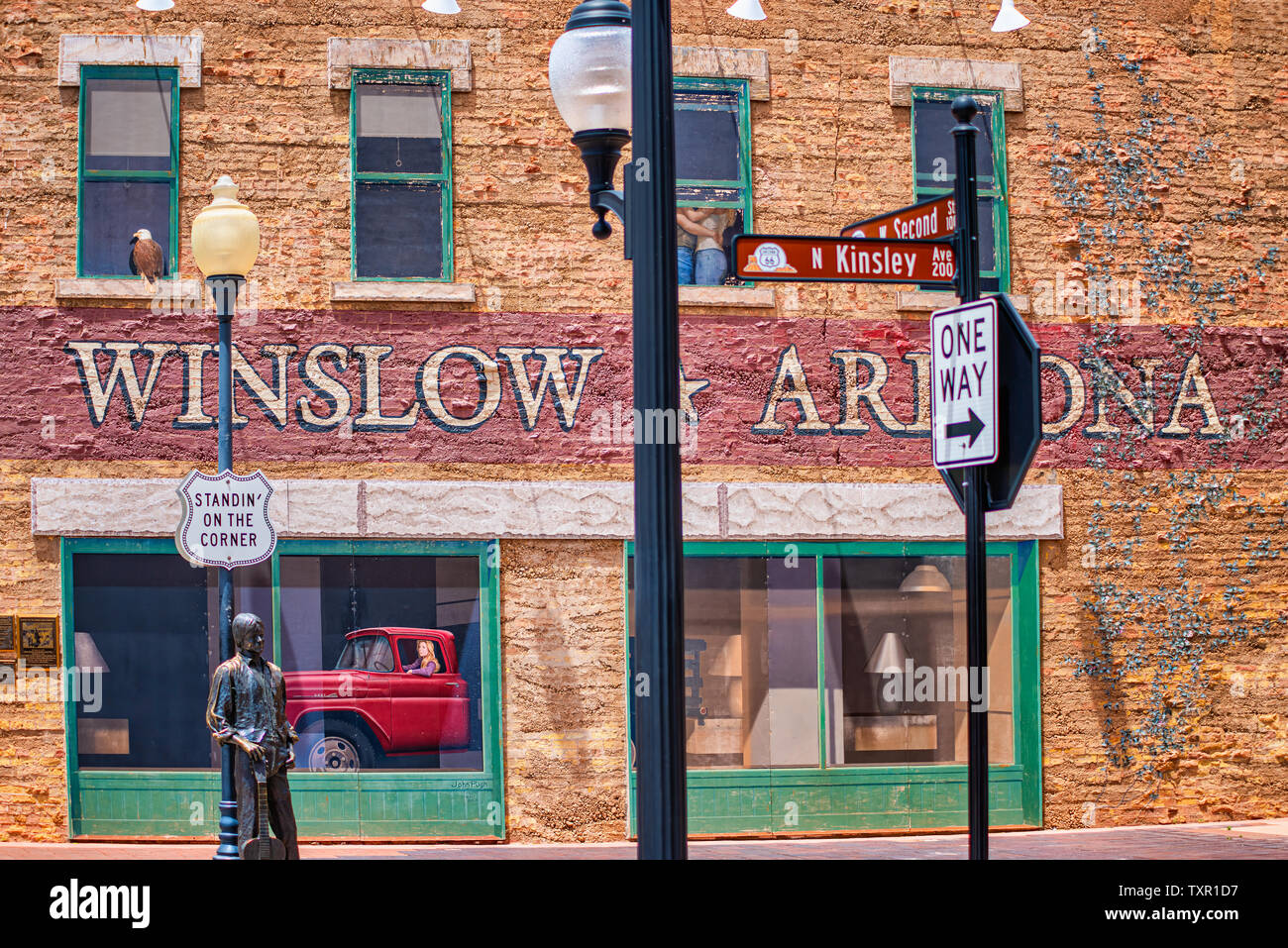 Winslow Arizona, USA 5/16/2016. Seite von Gebäude mit Kunst arbeiten, Windows, Menschen umarmen, Adler, Fahrzeug mit Fahrerin. Schilder, Statue Stockfoto