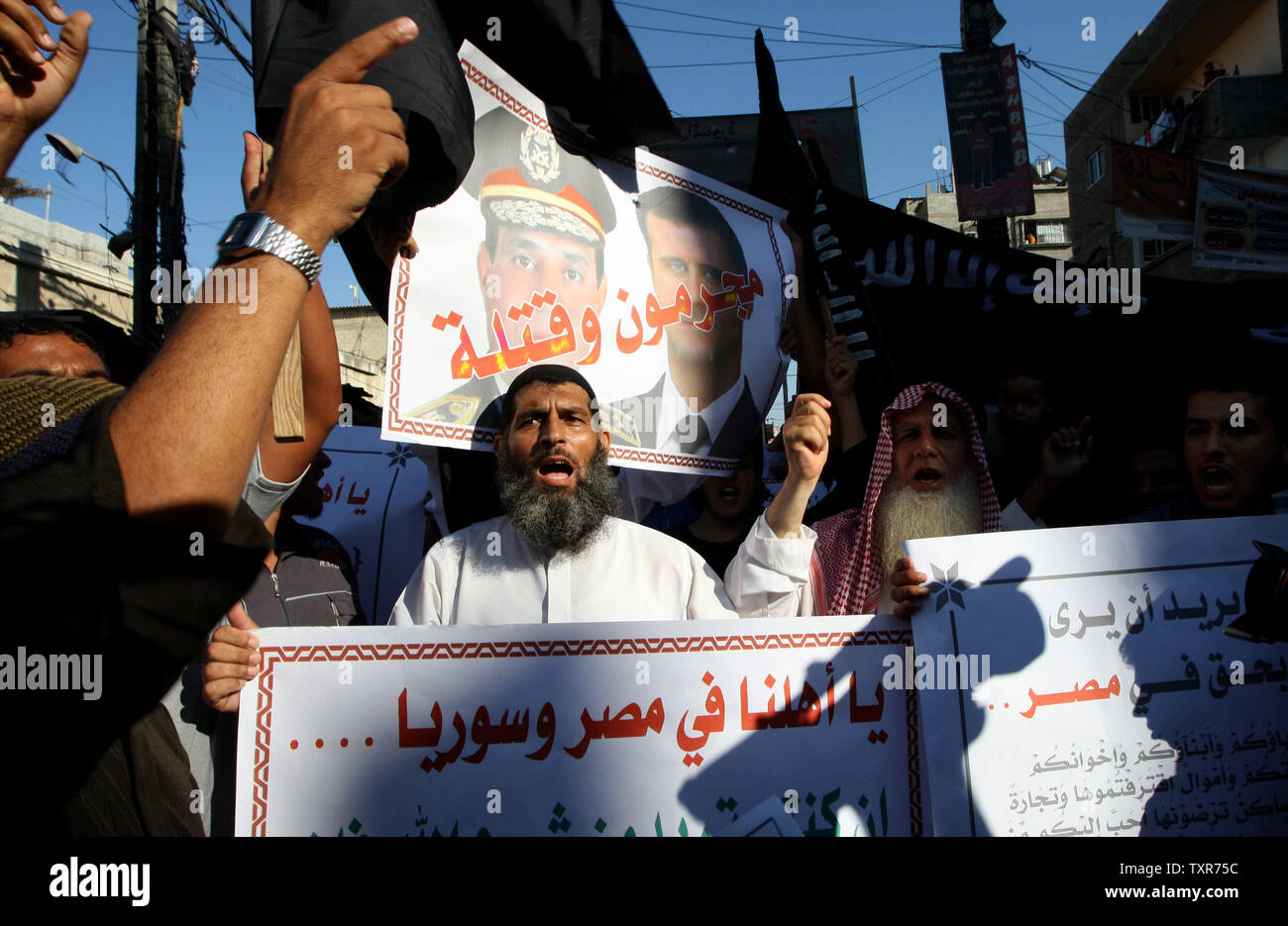 Eine palästinensische Salafistischen shouts Parolen vor einem Plakat mit Syrien Präsident Baschar al-Assad (R) und Ägyptens Armeechef General Abdel Fattah al-Sisi mit der arabischen Wörter, lesen ' Verbrecher und Mörder', während einer Kundgebung aus Protest gegen das, was sie sagen, sind die jüngsten Massaker gegen die syrische und ägyptische Volk begangen, in Rafah im südlichen Gazastreifen, 22. August 2013. UPI/Ismael Mohamad Stockfoto