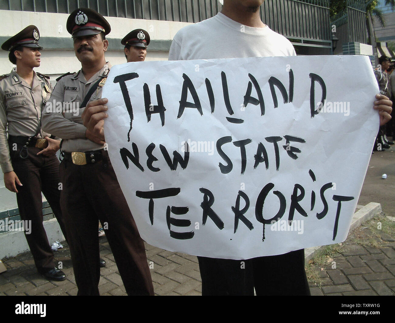 Ein Demonstrant hält ein Plakat als Polizist stand Guard während einer Demonstration vor der Thailändischen Botschaft in Jakarta, 29. Oktober 2000, die seniorenuniversität neue Tod von mindestens 84 muslimischen Aufständischen in der Provinz Narathiwat. Mindestens 200 Demonstranten zeigten ihre religiöse Solidarität und verurteilte die thailändische Polizei Aktion, die auf die große Zahl der Todesopfer geführt. (UPI/Newspictures Saprizal) Stockfoto