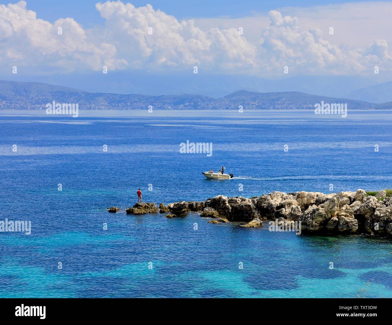 Ein Mann angeln von einigen Felsen in Kassiopi, Kassopaia, Ionische Inseln, Korfu, Griechenland Stockfoto