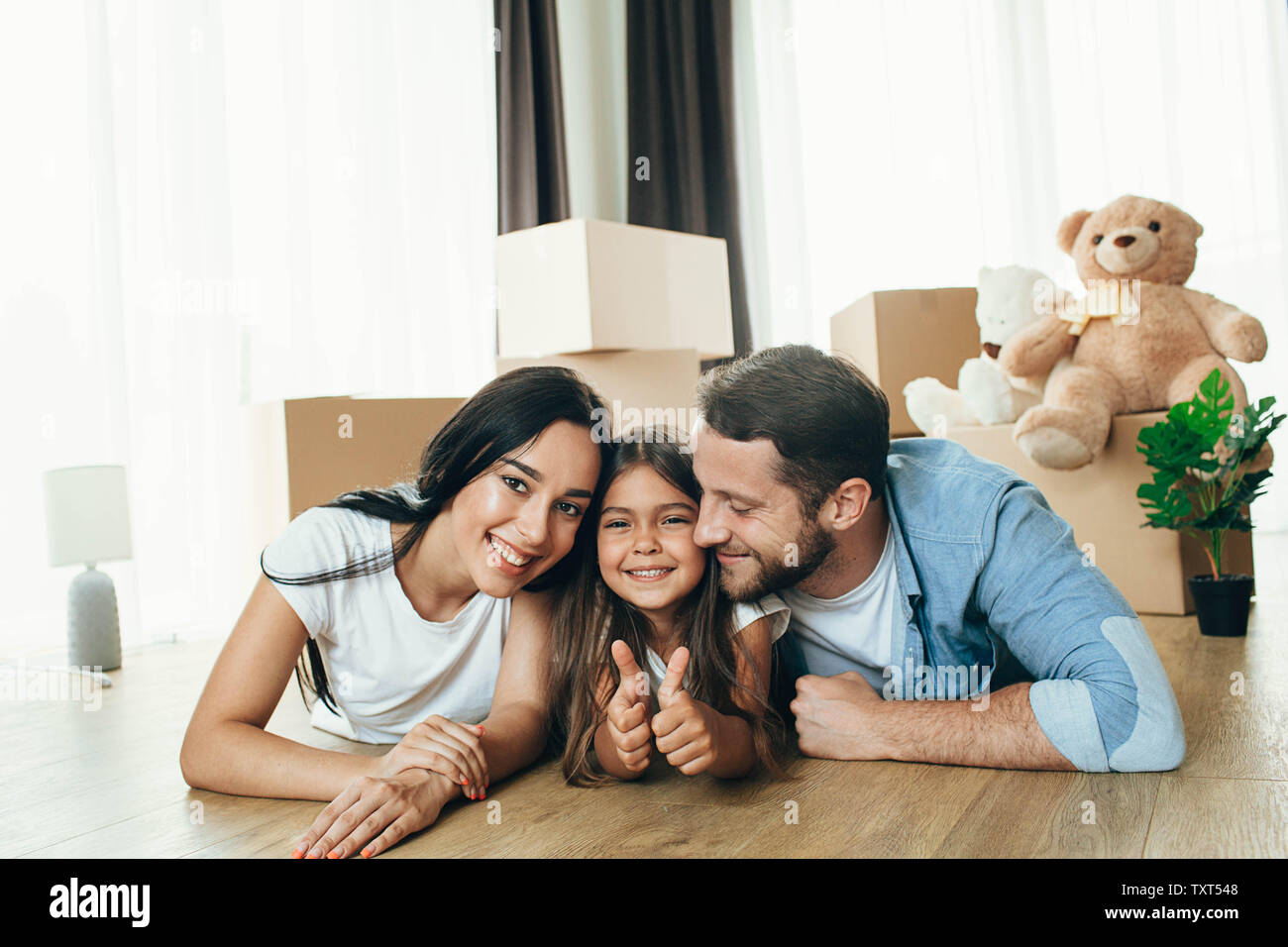 Glückliches Kind mit Familie, Daumen hoch in Ihrem neuen Haus. Es ist wunderbar, Umzug in eine neue Wohnung Stockfoto