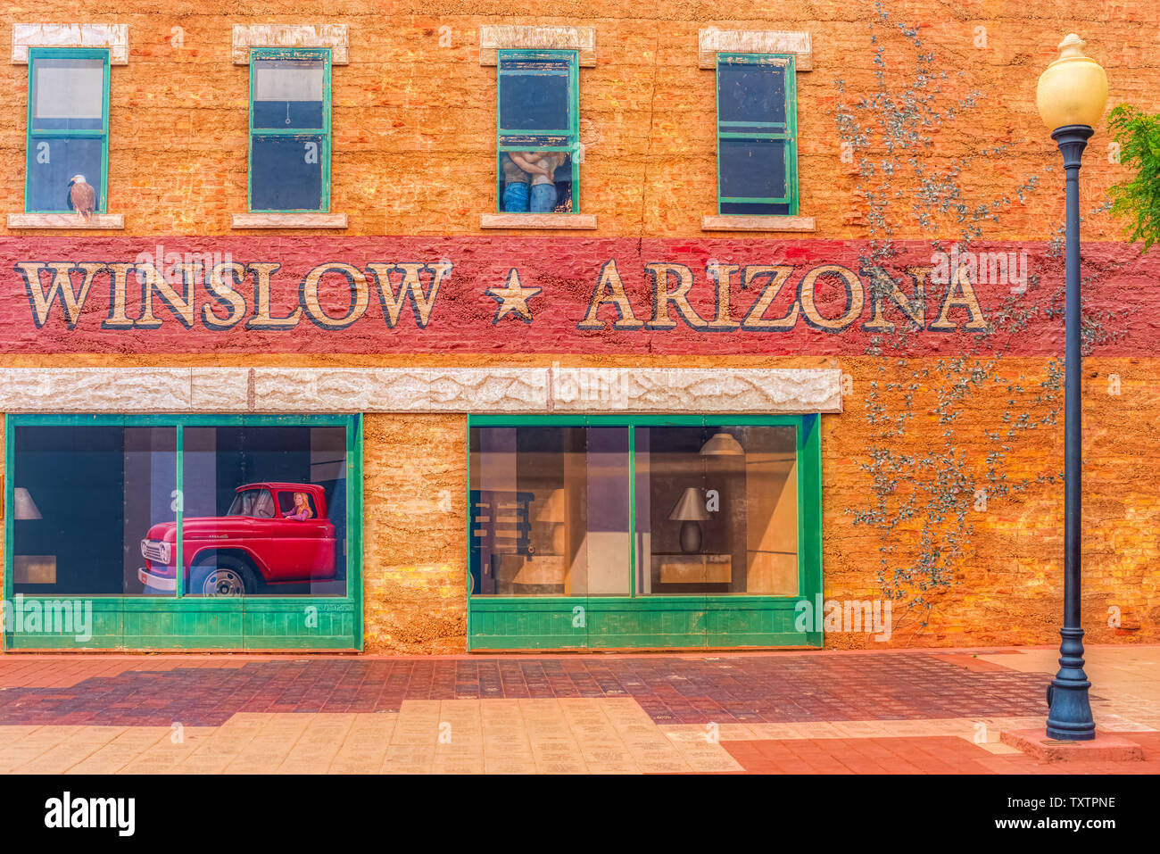 Winslow Arizona, USA 5/16/2016. Seite von Gebäude mit Kunst arbeiten, Windows, Menschen umarmen, Adler, LKW-Pritsche Ford mit weiblichen Treiber. Stockfoto