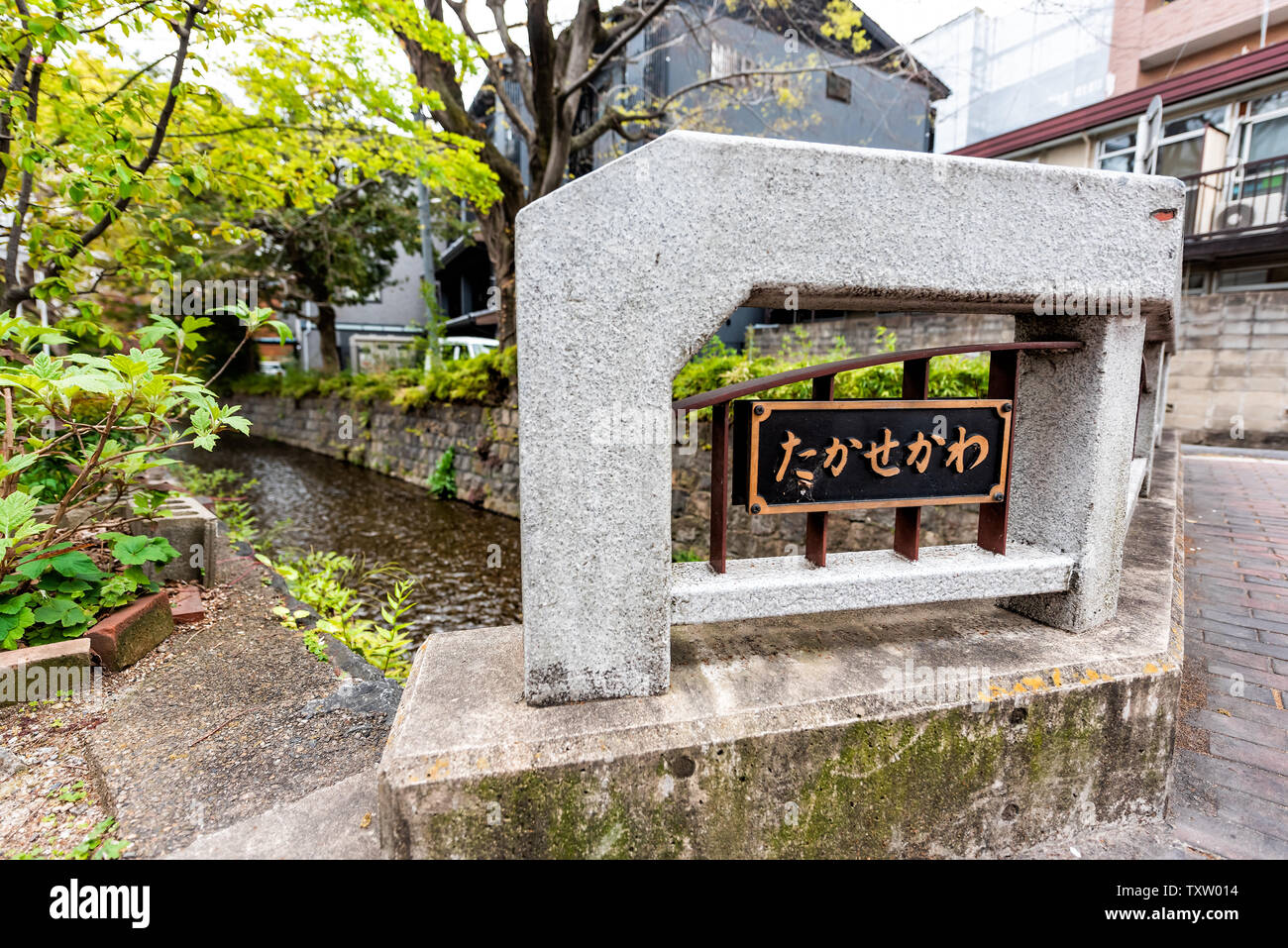 Kyoto Wohngegend im Frühjahr mit Vorzeichen in der japanischen Übersetzung für Takase Fluss Kanal Wasser im April in Japan mit grünen Bäumen, Pflanzen Stockfoto