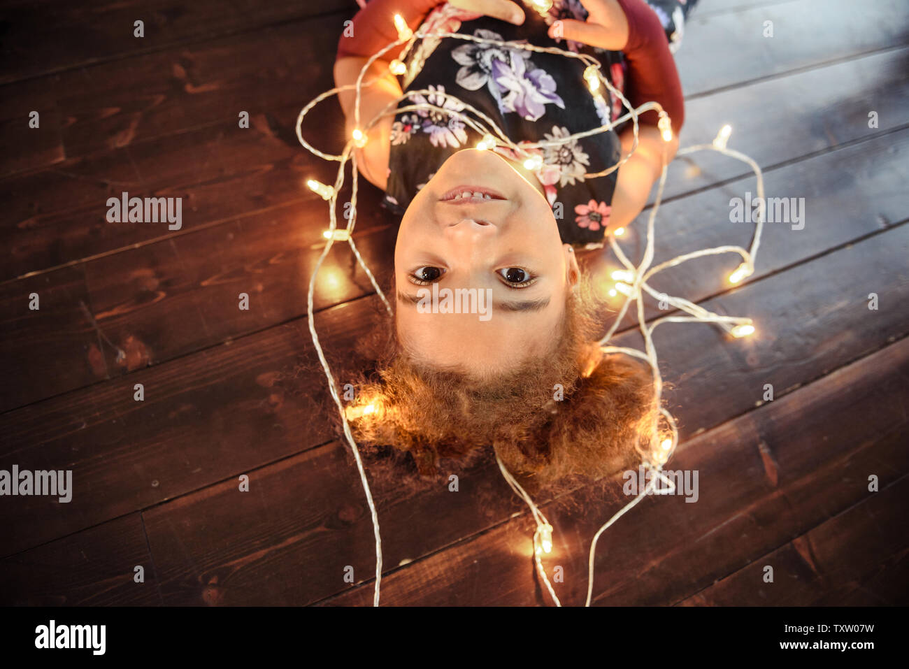 Süße kleine Mädchen mit auf Flor mit hellen christmas garland in ihrem Haar. Weihnachten Portrait, gemütlicher Stil. Ansicht von oben. Stockfoto