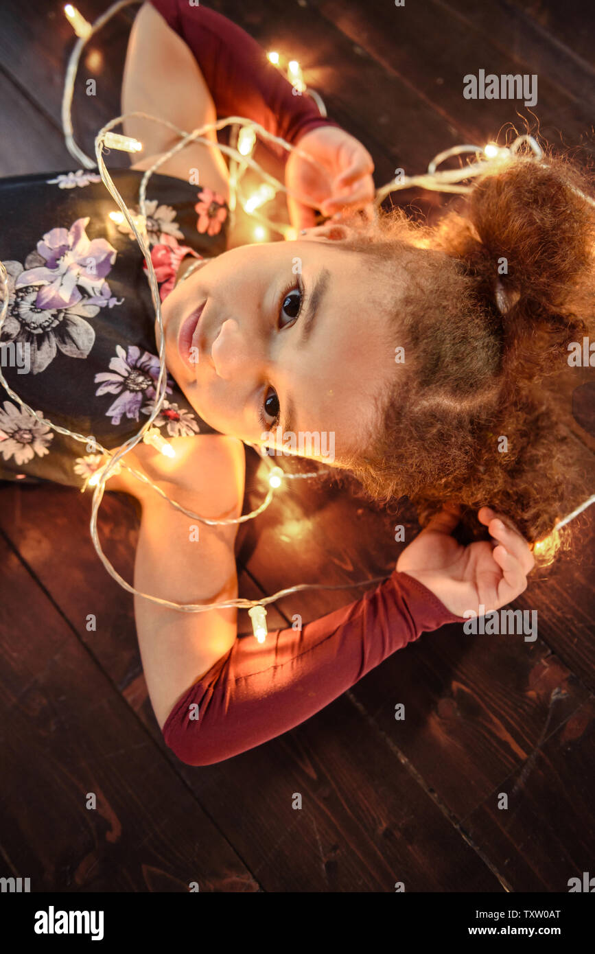Süße kleine Mädchen mit auf Flor mit hellen christmas garland in ihrem Haar. Weihnachten Portrait, gemütlicher Stil. Ansicht von oben. Stockfoto