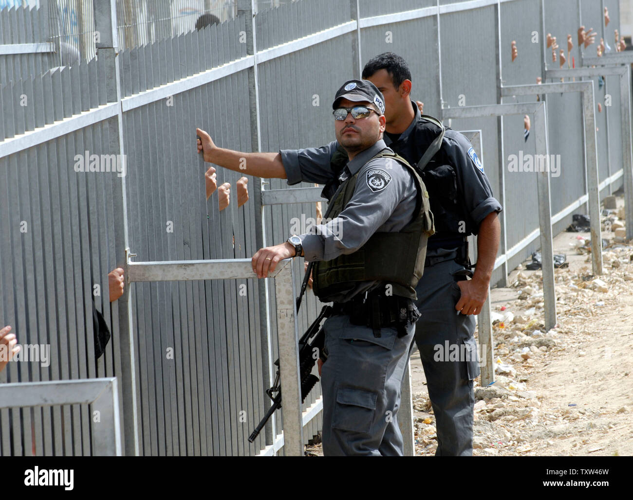 Israelische Grenzpolizisten stand durch einen Zaun ausblenden Palästinenser wartet das israelische Militär checkpoint aus Bethlehem, 5. Oktober 2007, nach Jerusalem zu überqueren. Ein israelischer Schließung auf der West Bank dürfen nur Männer über 50 Jahre und Frauen über 40 Jahre alt Geben Sie Jerusalem an der Al Aqsa Moschee, die drittheiligste Ort des Islam zu beten, für Ramadan Freitag Gebeten. (UPI Foto/Debbie Hill) Stockfoto