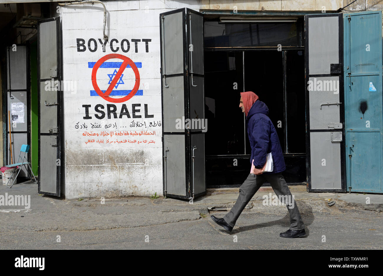 Eine palästinensische Spaziergänge durch Graffiti lesen "Boykott Israel" am Eingang des Beit Jibrin Flüchtlingslager in Bethlehem, West Bank, 11. Februar 2015. Ein hohes Niveau der Nationalen Palästinensischen Ausschuss gab es Geschäfte in der West Bank angewiesen hat Produkte von sechs großen israelischen Unternehmen sind: Tnuva, die Strauss Group, Osem, Elite und Prigate Jafora-Tabori zu verbieten. Das Verbot soll Israels Entscheidung der Verweigerung des palästinensischen Steuereinnahmen sammelt er im Namen der Palästinensischen Autonomiebehörde Gegenmaßnahme. West Bank Lebensmittelgeschäft muss den Verkauf von israelischen Produkten innerhalb von zwei Wochen von heute. P Stockfoto