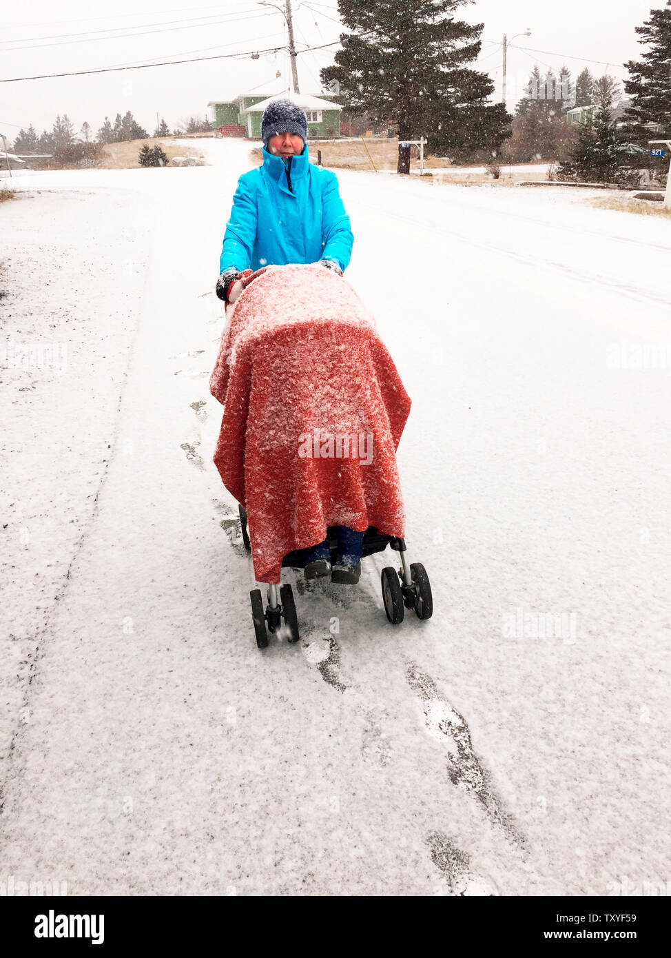 Eine Frau mit einem Kinderwagen, der an einem Wintertag mit einer Decke bedeckt ist, während überall Neuschnee fällt, Halifax, Kanada. Oma auf einem Ausflug. Stockfoto