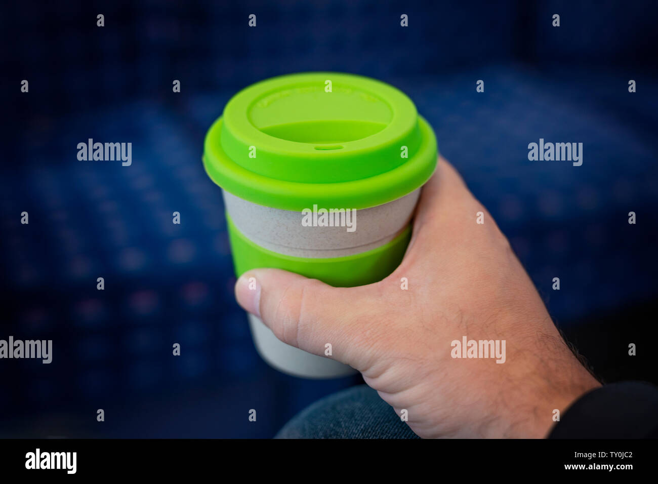 Ein Mann hält eine wiederverwendbare Kaffeetasse, während auf einem Zug saß. Stockfoto