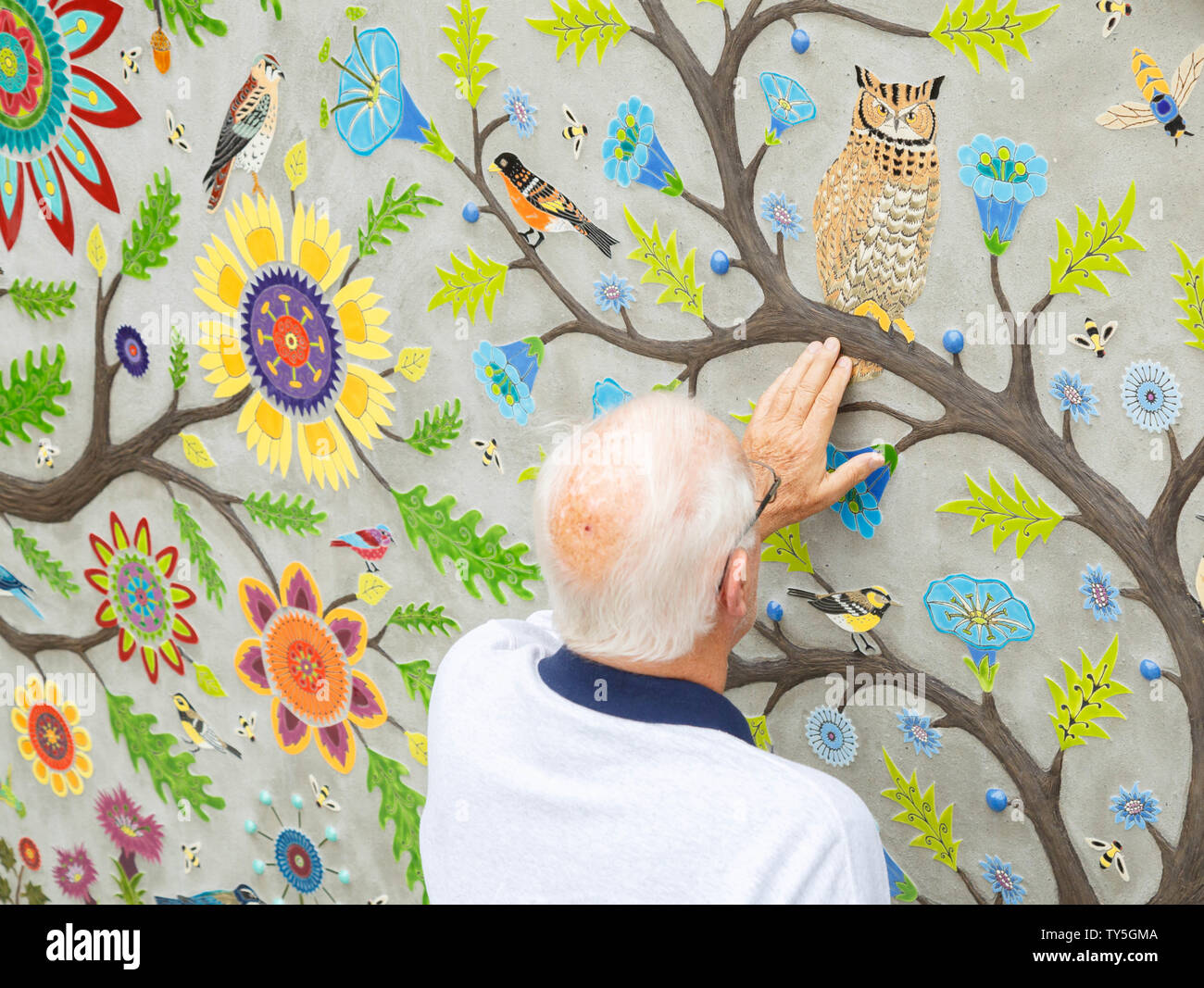 Ein älterer Mann Adel berührt das Wandbild mit angehobenen Putz und farbenfrohen Designs am Pike Place Market, Seattle, USA gemalt. Stockfoto