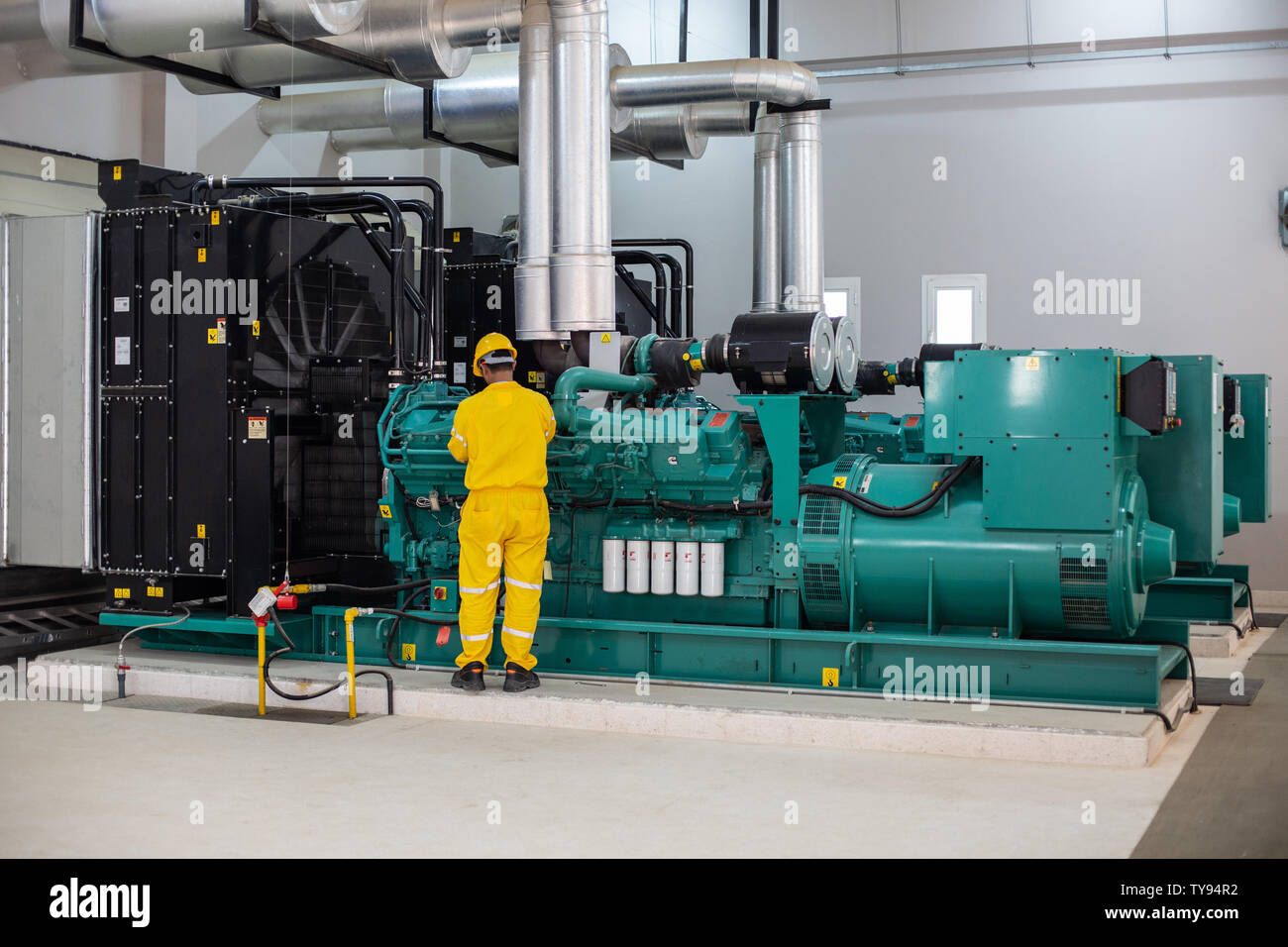 Männer, die an einem grünen Dieselgenerator arbeiten, der ein gelbes Arbeitskleid trägt, verwenden alle Sicherheitsmaßnahmen mit einer sauberen Umgebung, um das Risiko zu verringern Stockfoto
