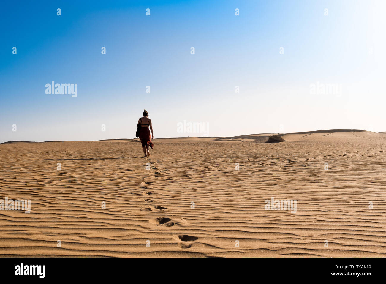 Junge selbstbewusste Frau alleine auf Wüste Sand unter den Dünen an einem heißen sonnigen Tag mit blauen Himmel Stockfoto