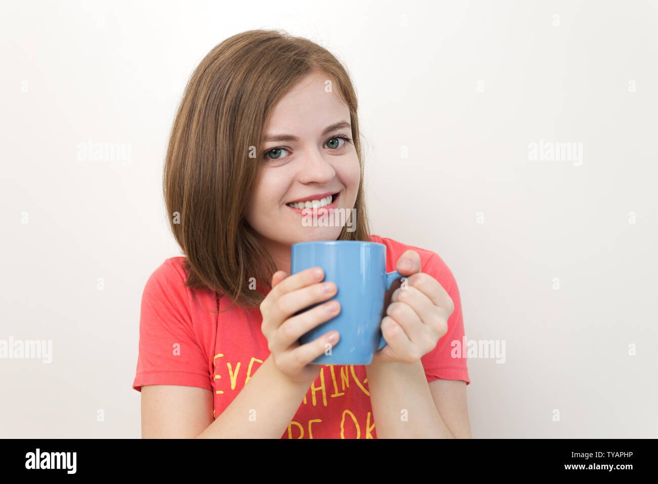 Portrait von lächelnden jungen kaukasischen Frau Mädchen mit einem Becher Kaffee mit beiden Händen, als ob sagen: Guten Morgen! Stockfoto