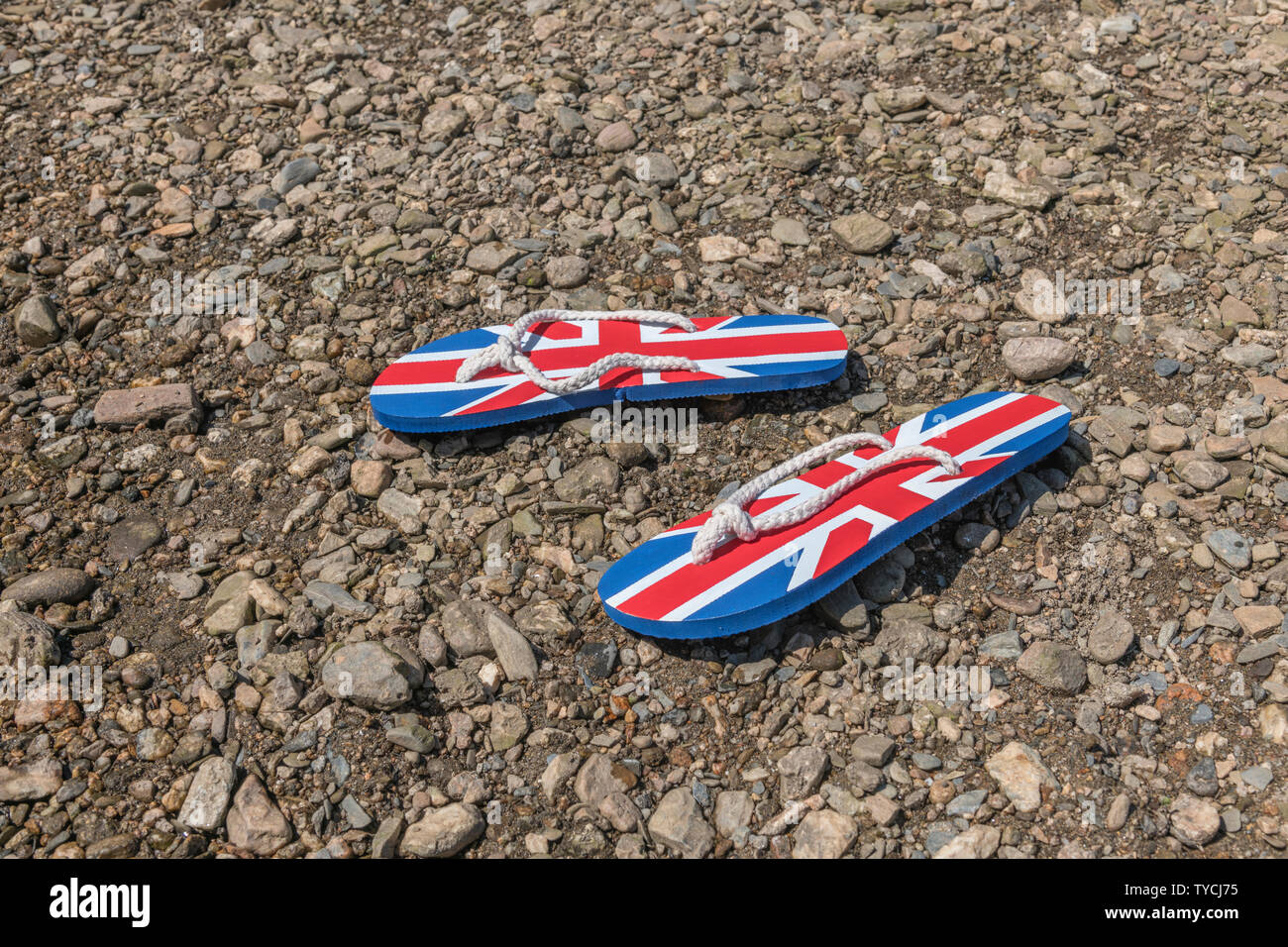 Union Jack Flip-Flops auf River Shingle - Metapher 2021 Aufenthalt in Großbritannien, Urlaub zu Hause, Aufenthalt in Cornwall, Landurlaub, Flip-Flop-Schuhe. Stockfoto