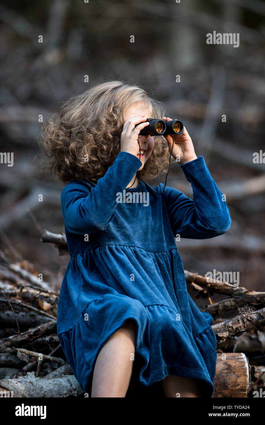 Stilvolle kind Mädchen 6-7 Jahre alt tragen Designer Blue Velvet Dress in Wald. Im Freien. Standortwahl und Spielen mit dem Fernglas. Kindheit. Stockfoto