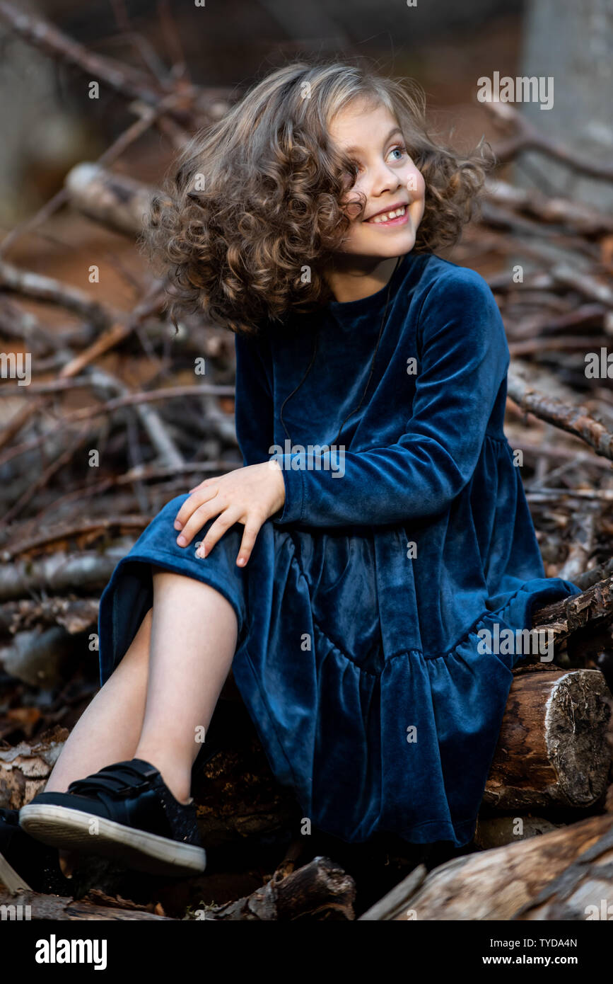Stilvolle kind Mädchen 6-7 Jahre alt tragen Designer Blue Velvet Dress in Wald. Im Freien. Standortwahl und lächelnd. Kindheit. Stockfoto